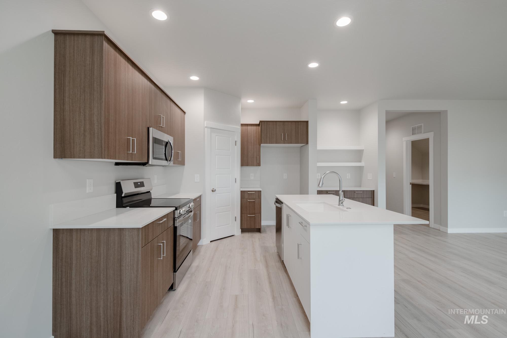 Kitchen with stainless steel appliances, light wood-style flooring, recessed lighting, modern cabinets, and a kitchen island with sink