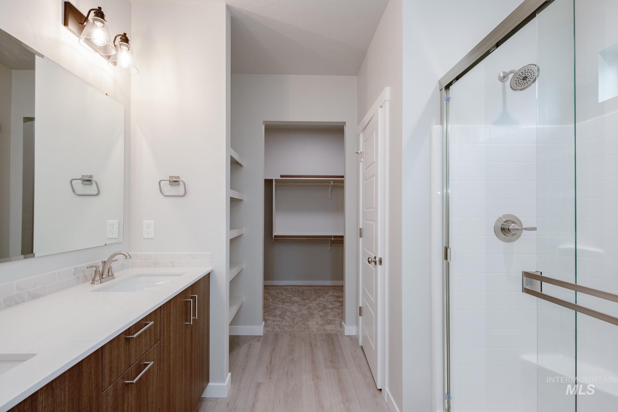 Full bathroom with double vanity, light wood-style flooring, a shower stall, and a spacious closet