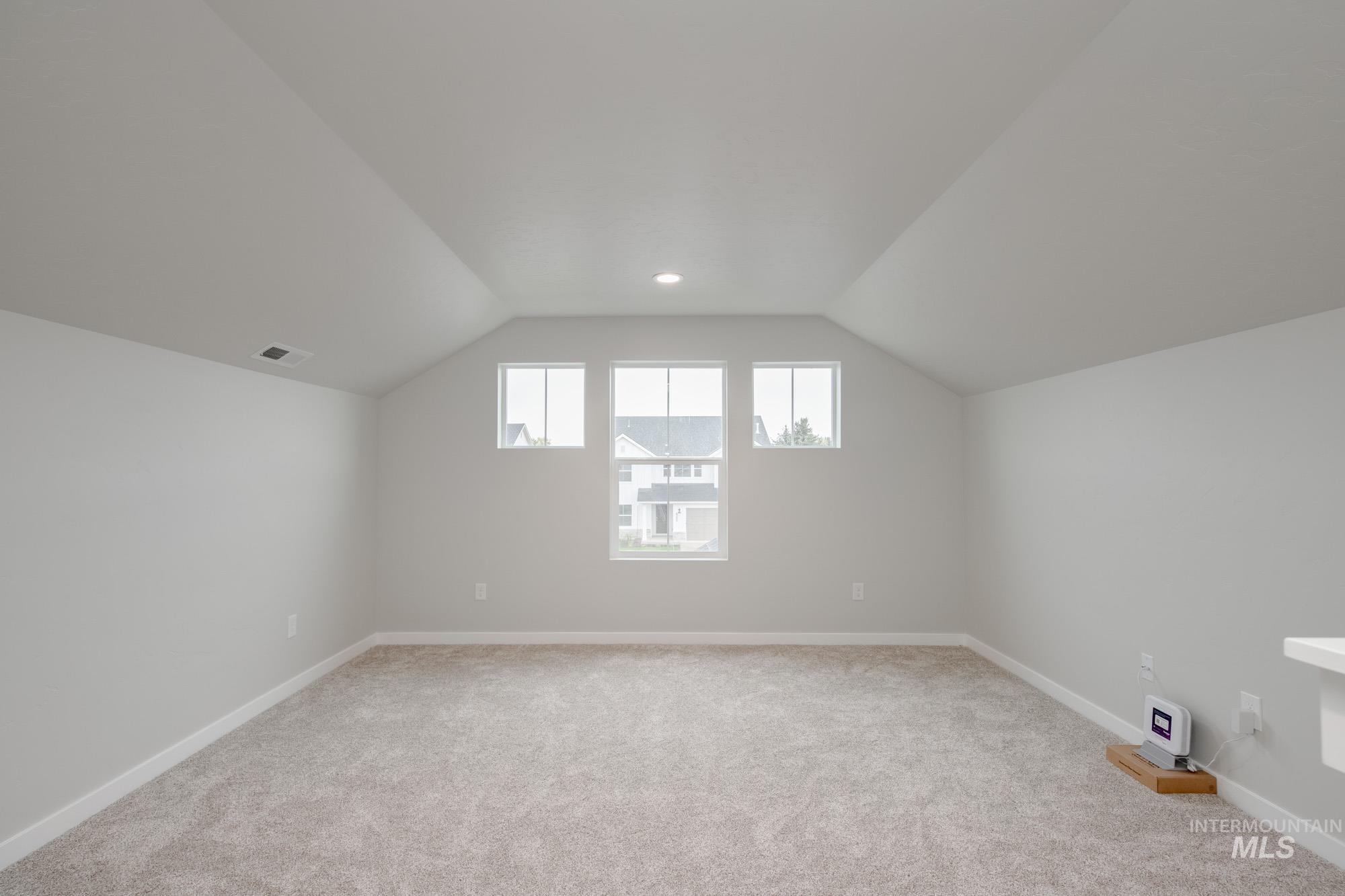 Bonus room with light carpet and vaulted ceiling