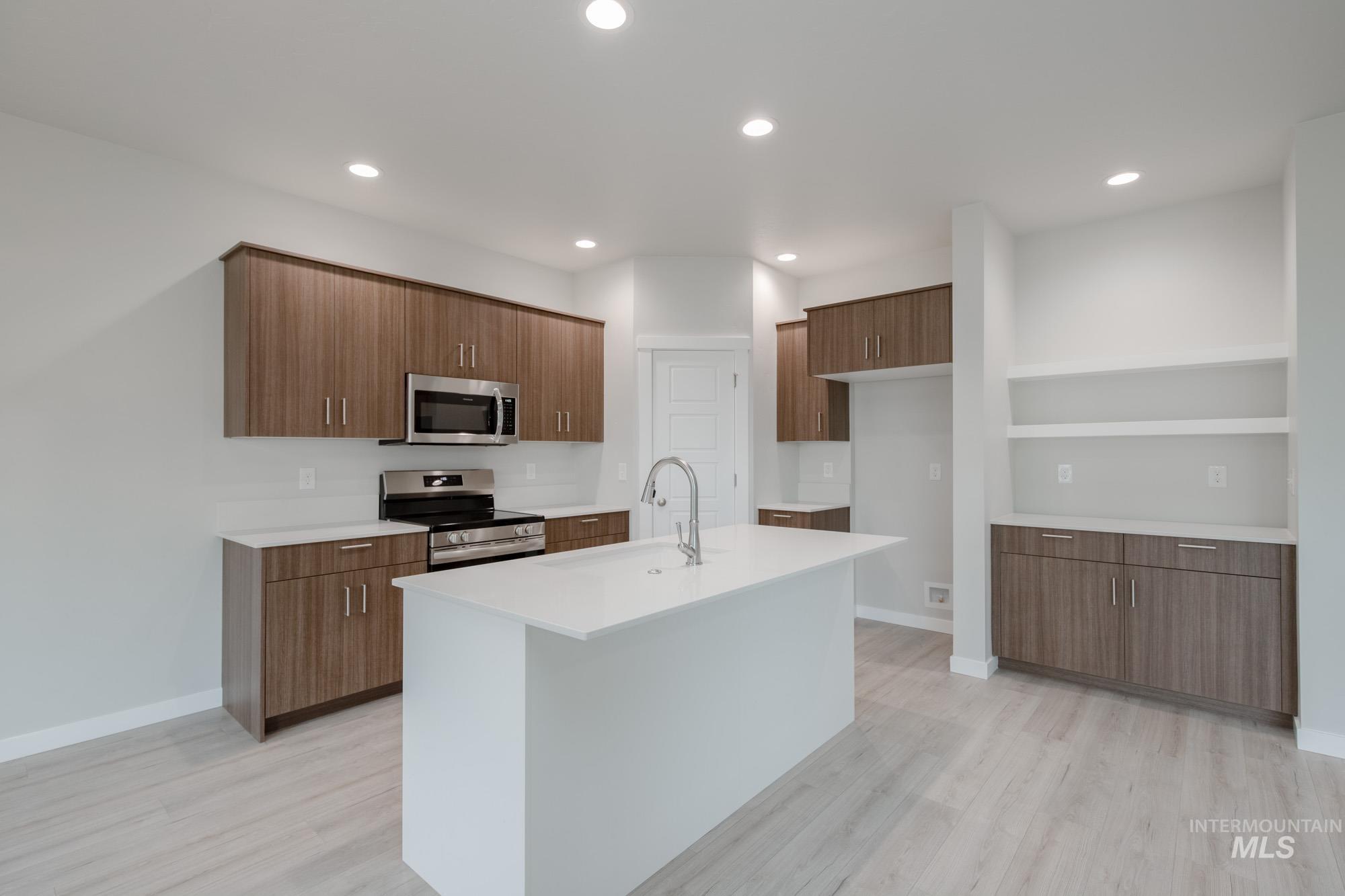 Kitchen featuring appliances with stainless steel finishes, recessed lighting, light wood finished floors, open shelves, and a center island with sink