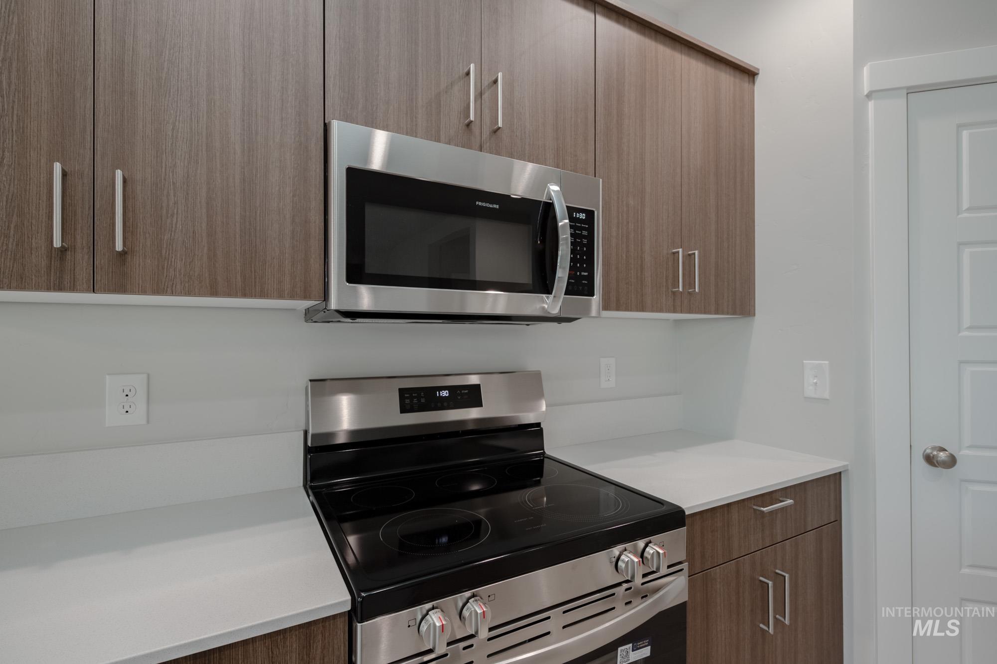 Kitchen featuring modern cabinets, appliances with stainless steel finishes, brown cabinets, and light stone counters