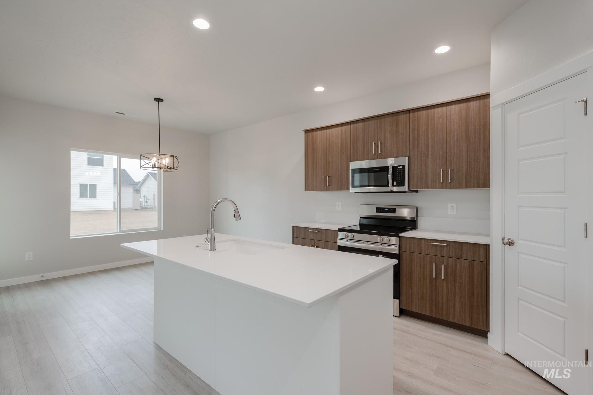 Kitchen featuring decorative light fixtures, appliances with stainless steel finishes, recessed lighting, an island with sink, and brown cabinetry