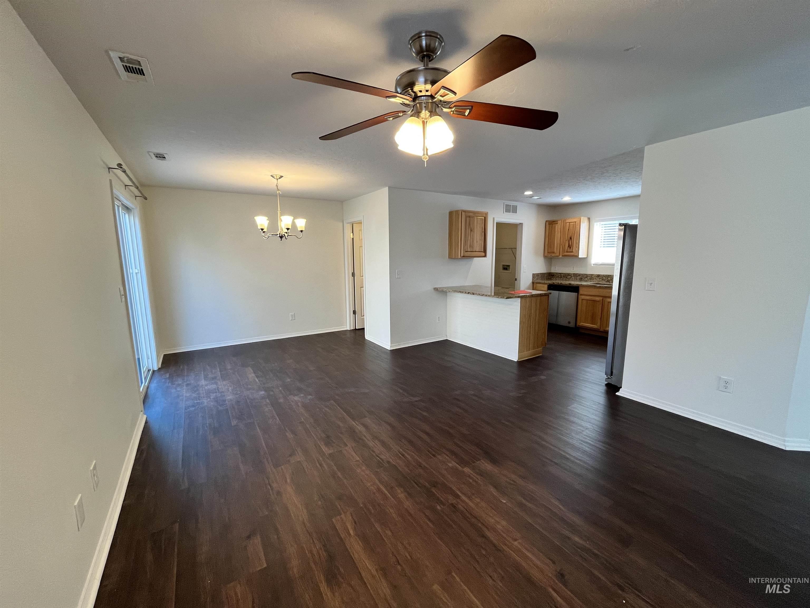 Unfurnished living room with dark wood-style flooring, ceiling fan, and a chandelier