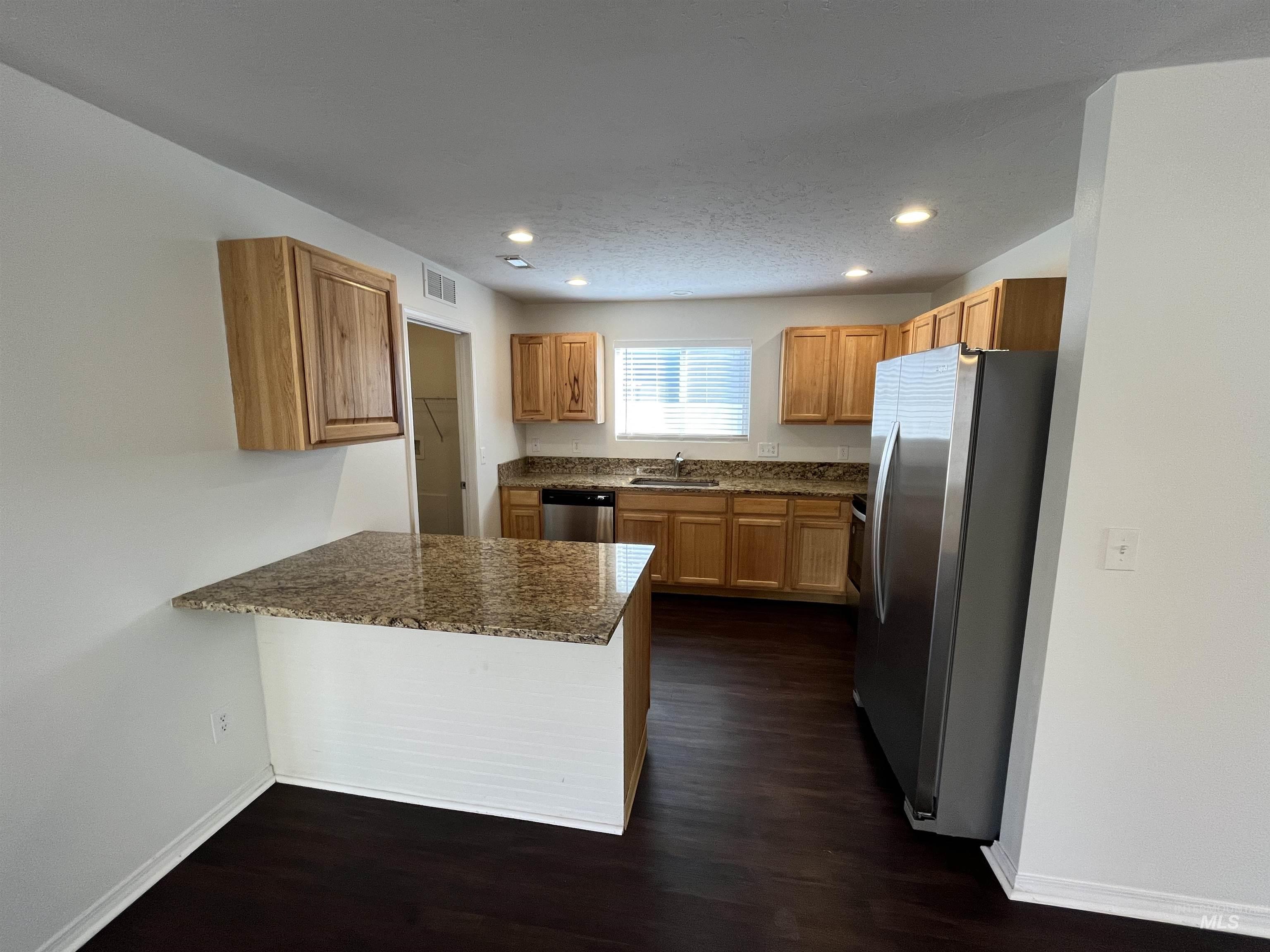 Kitchen featuring dark stone counters, stainless steel appliances, dark wood-type flooring, recessed lighting, and a peninsula