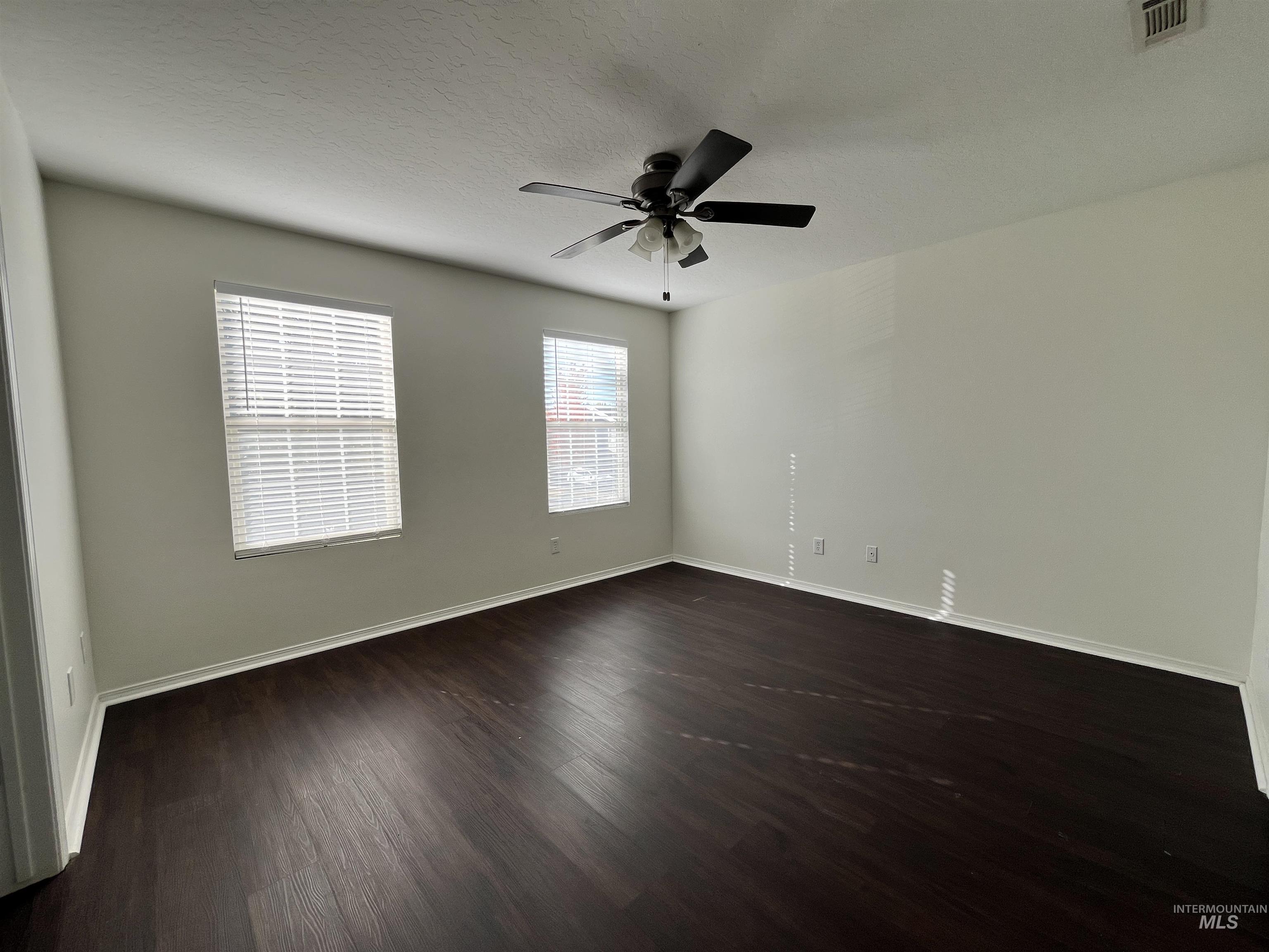 Empty room with dark wood-style flooring, a textured ceiling, and a ceiling fan