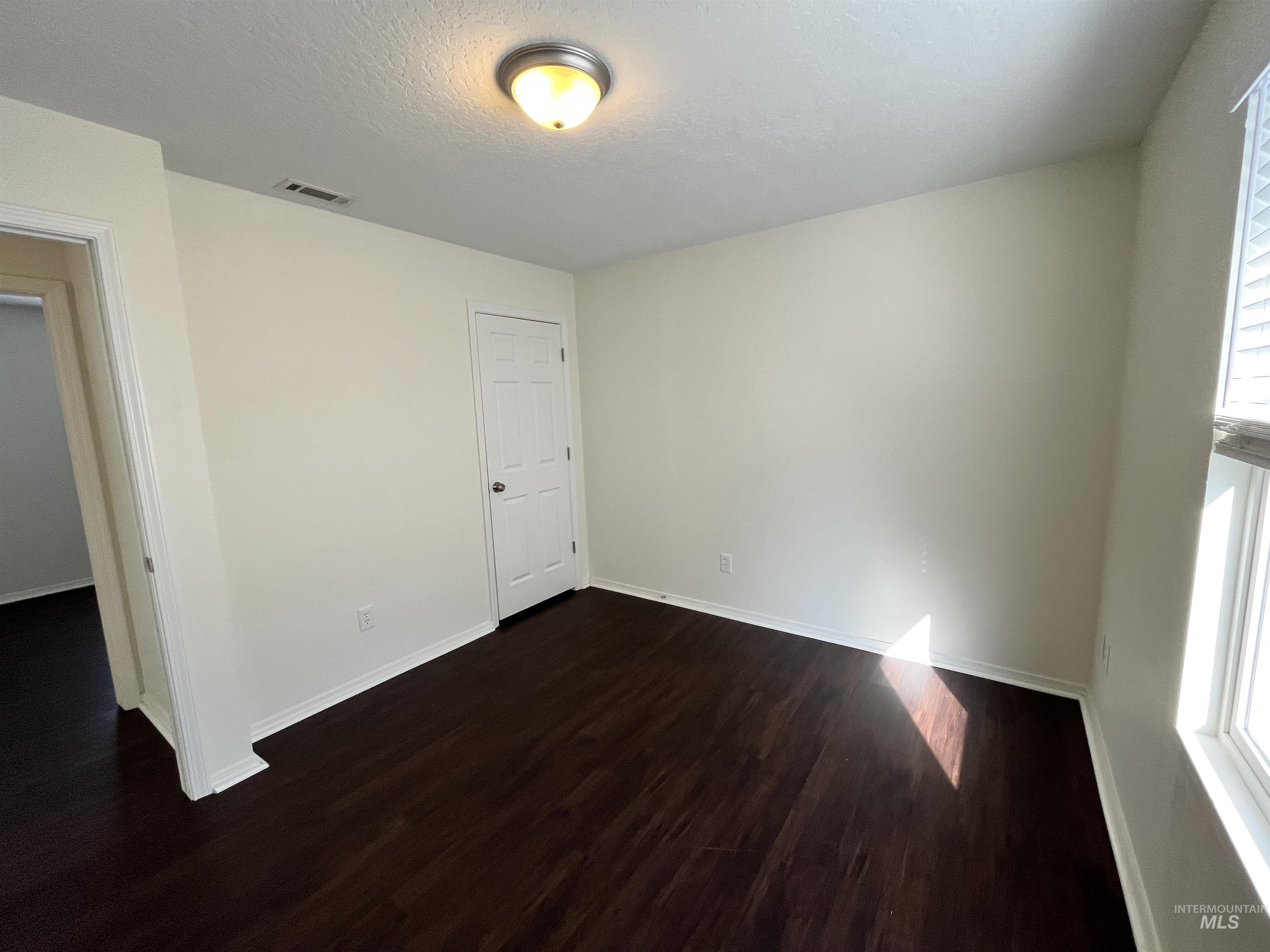 Empty room featuring dark wood-type flooring and a textured ceiling