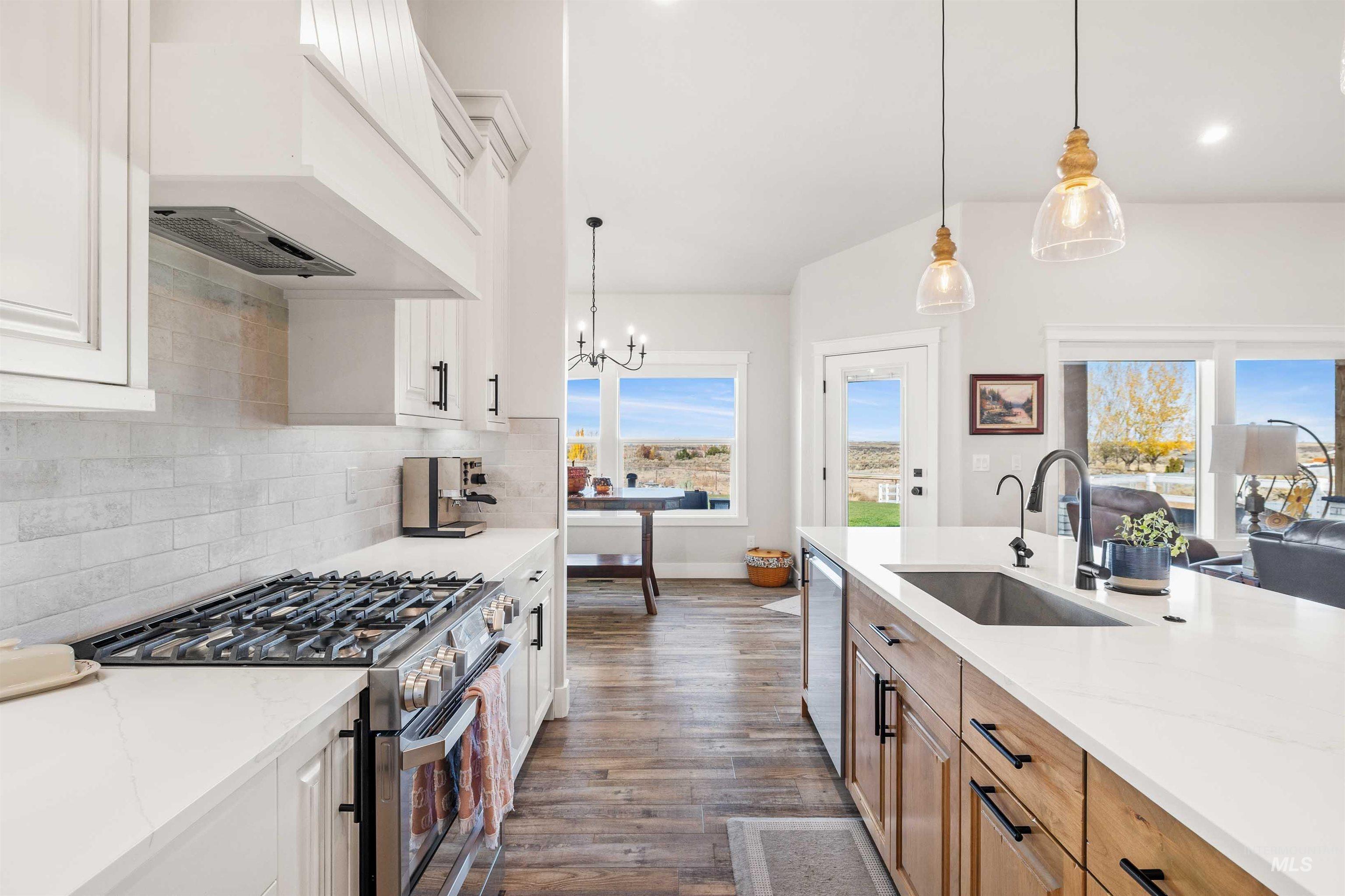 Kitchen with stainless steel appliances, pendant lighting, white cabinets, dark wood finished floors, and light stone counters