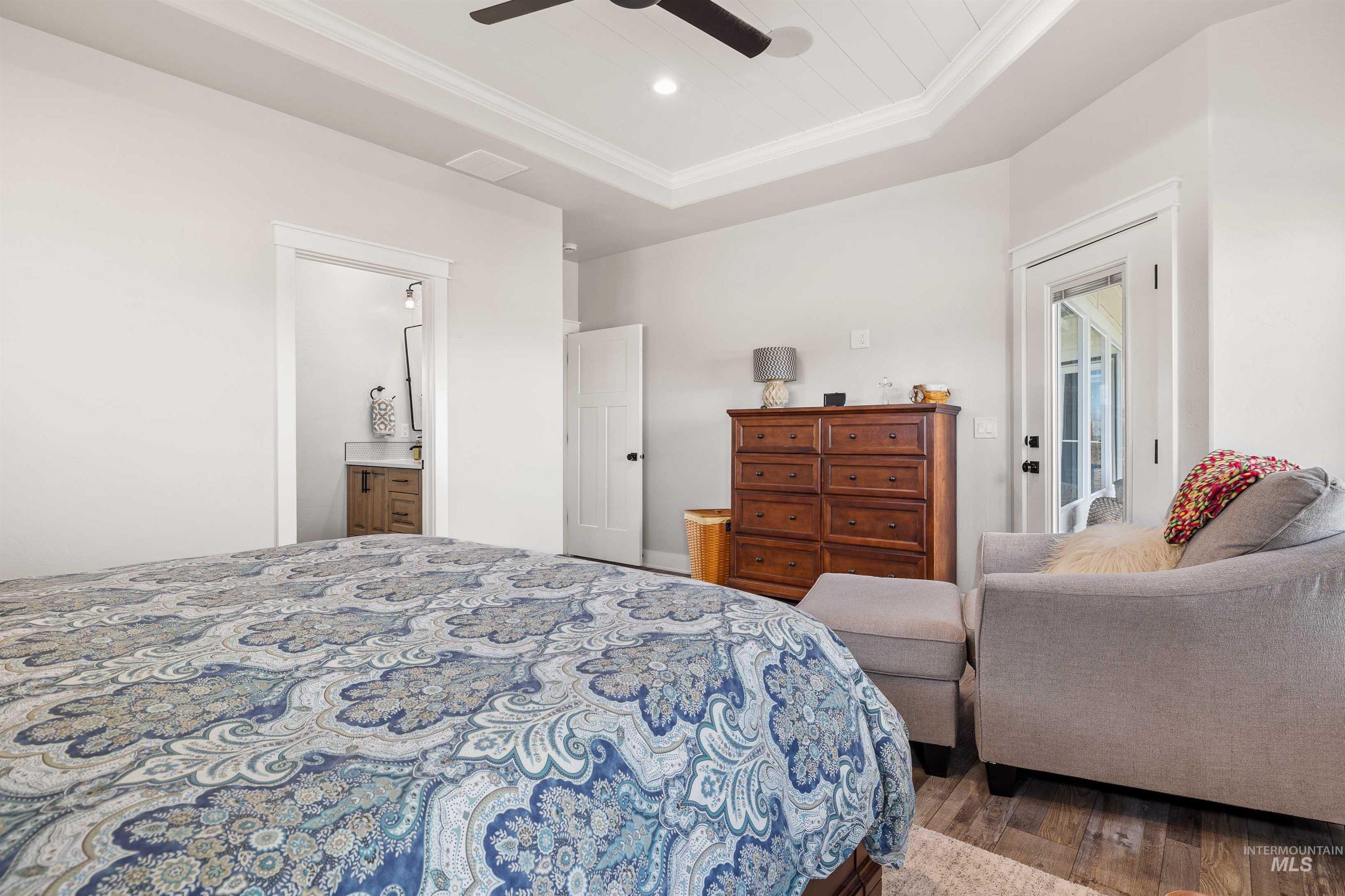 Bedroom featuring crown molding, wood finished floors, a tray ceiling, ceiling fan, and ensuite bathroom
