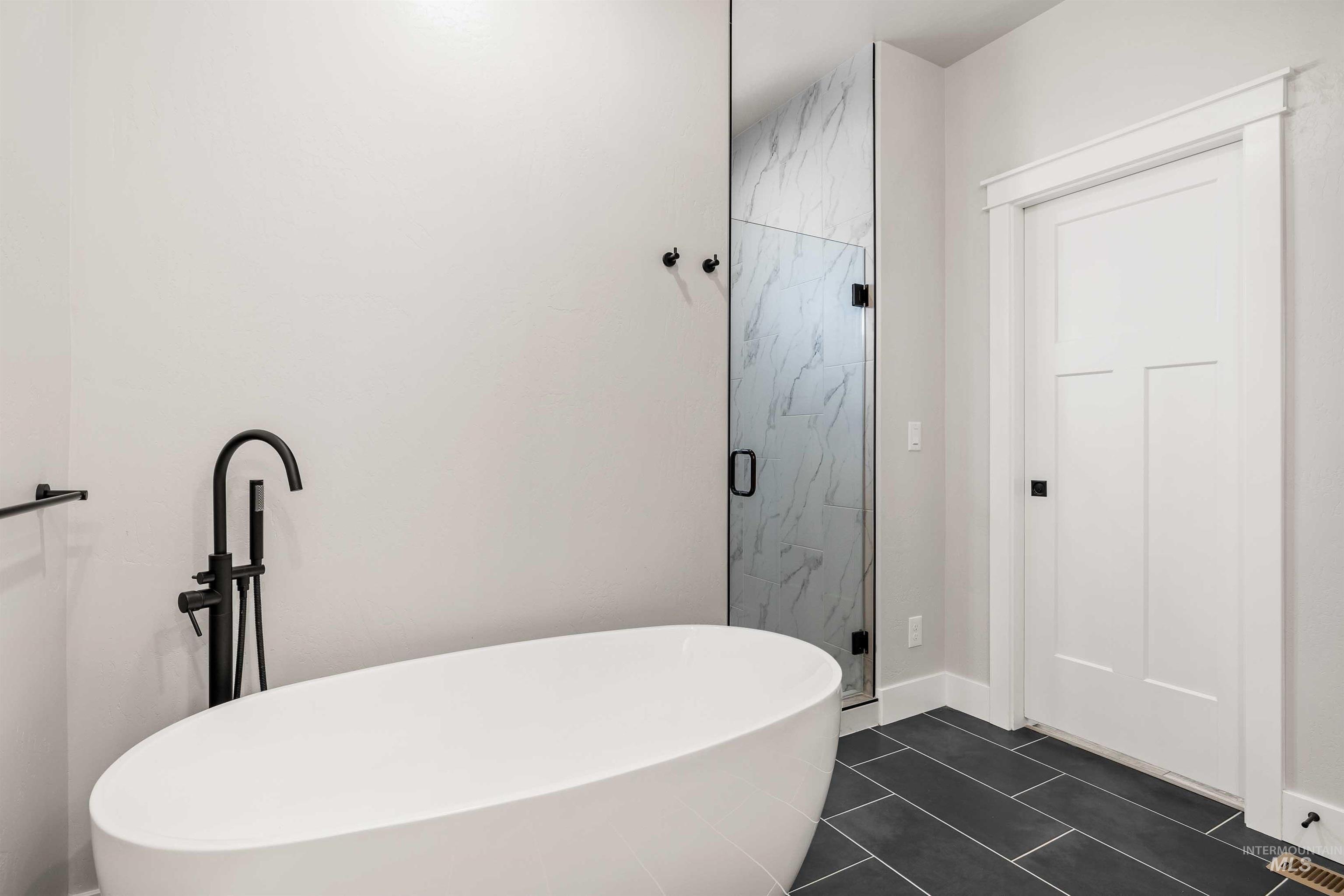 Full bathroom with dark tile patterned flooring, a marble finish shower, and a soaking tub