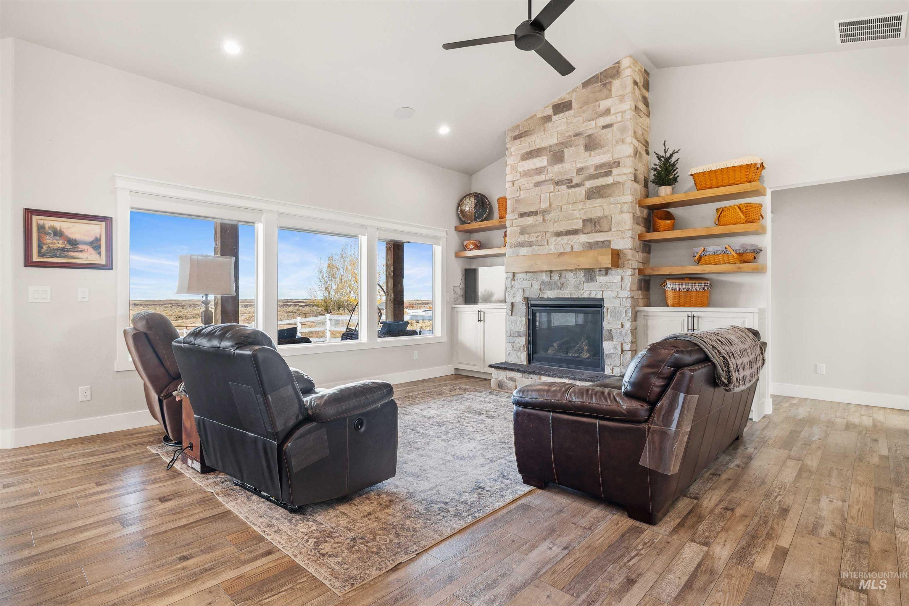 Living room with a stone fireplace, light wood finished floors, recessed lighting, a ceiling fan, and high vaulted ceiling