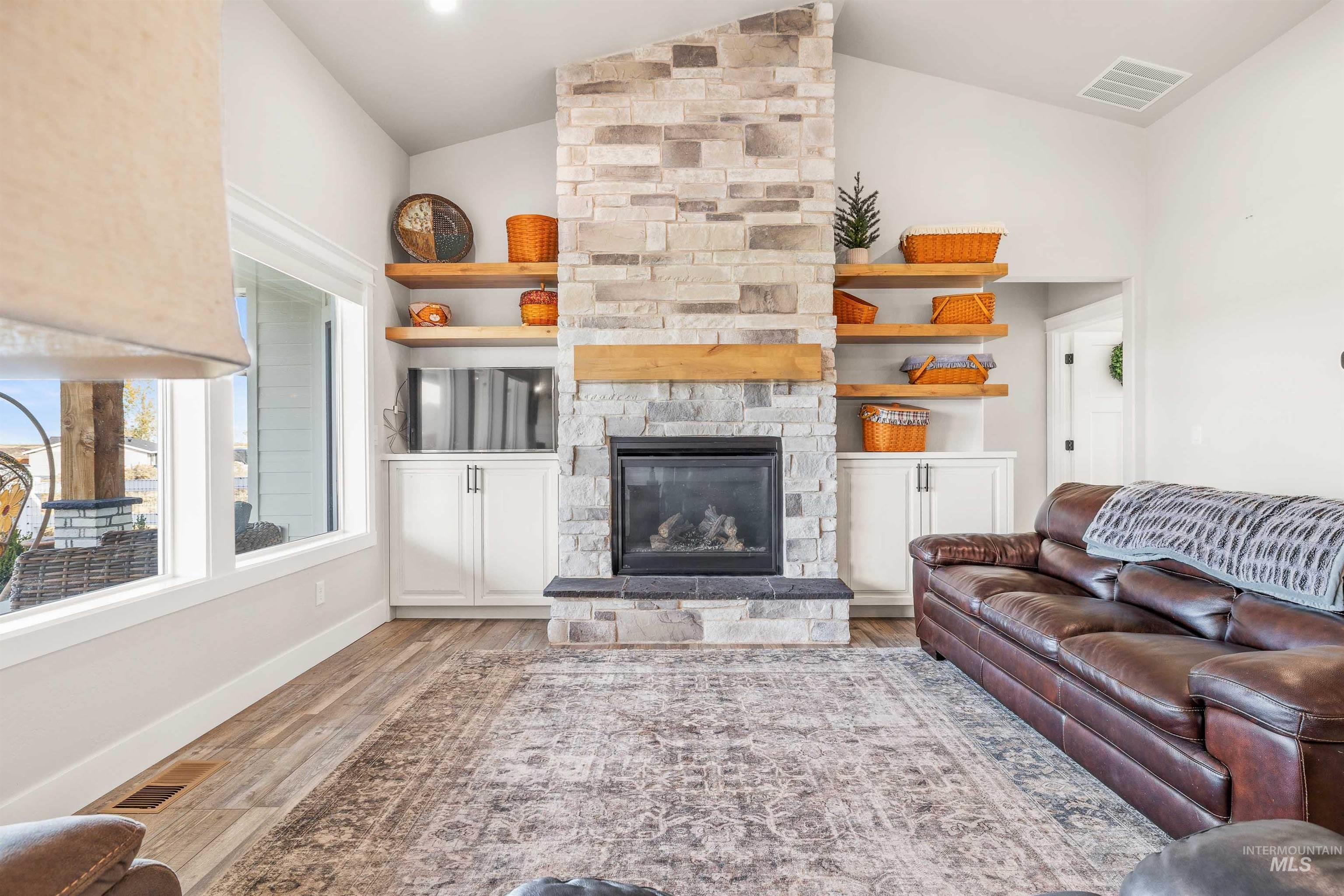 Living area with a stone fireplace, wood finished floors, and high vaulted ceiling