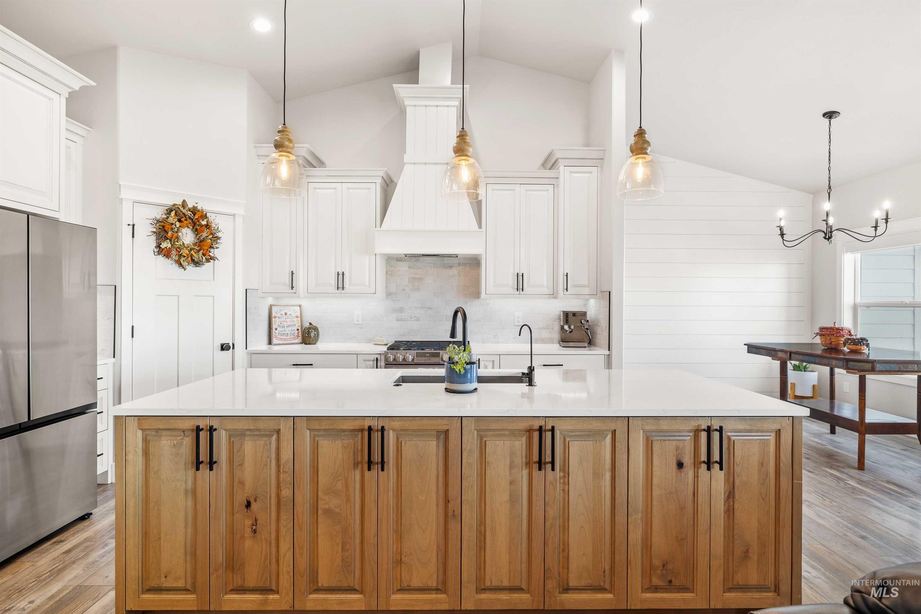 Kitchen with hanging light fixtures, light wood-style floors, freestanding refrigerator, light stone countertops, and high vaulted ceiling