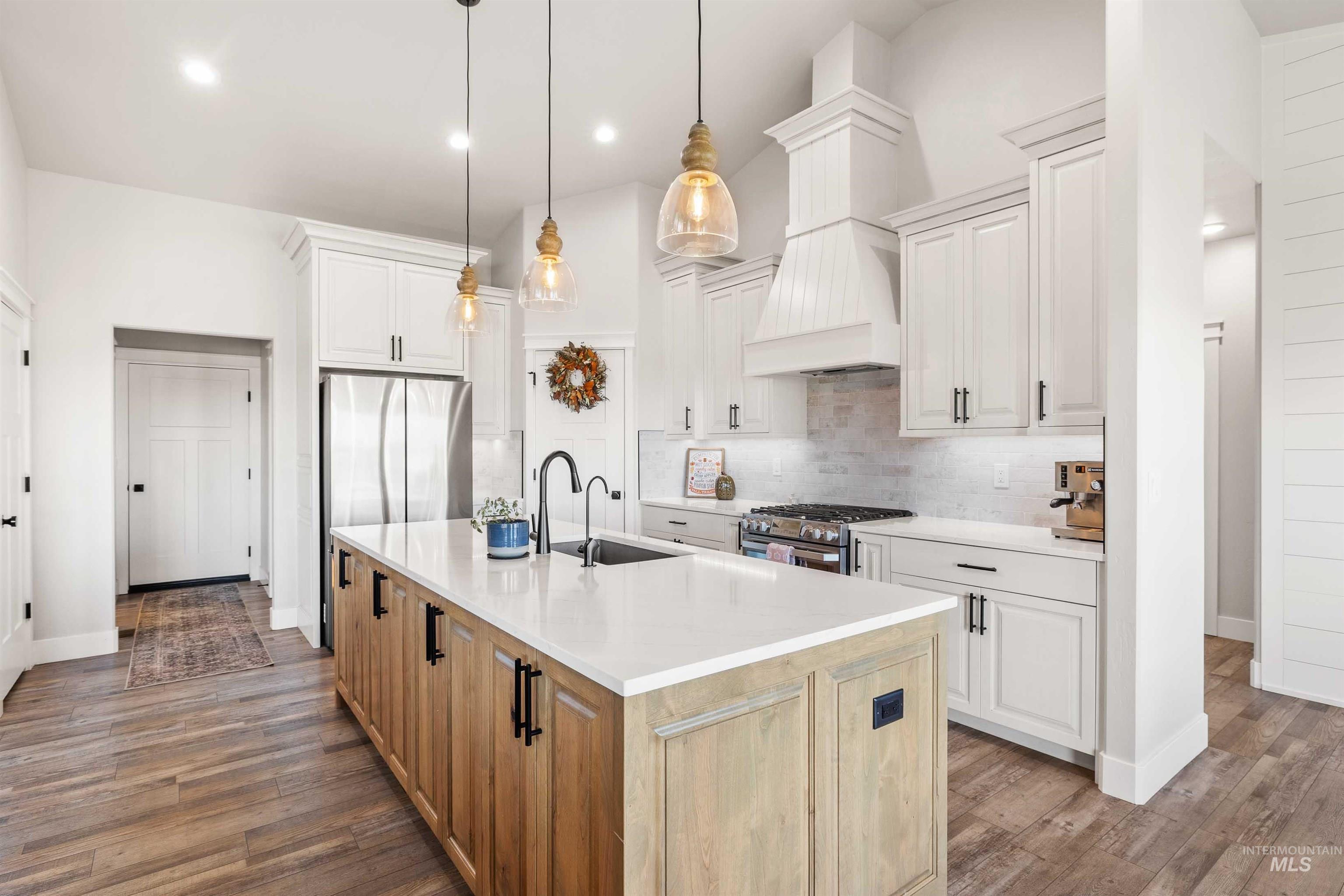 Kitchen with a center island with sink, dark wood-style floors, light stone countertops, hanging light fixtures, and backsplash