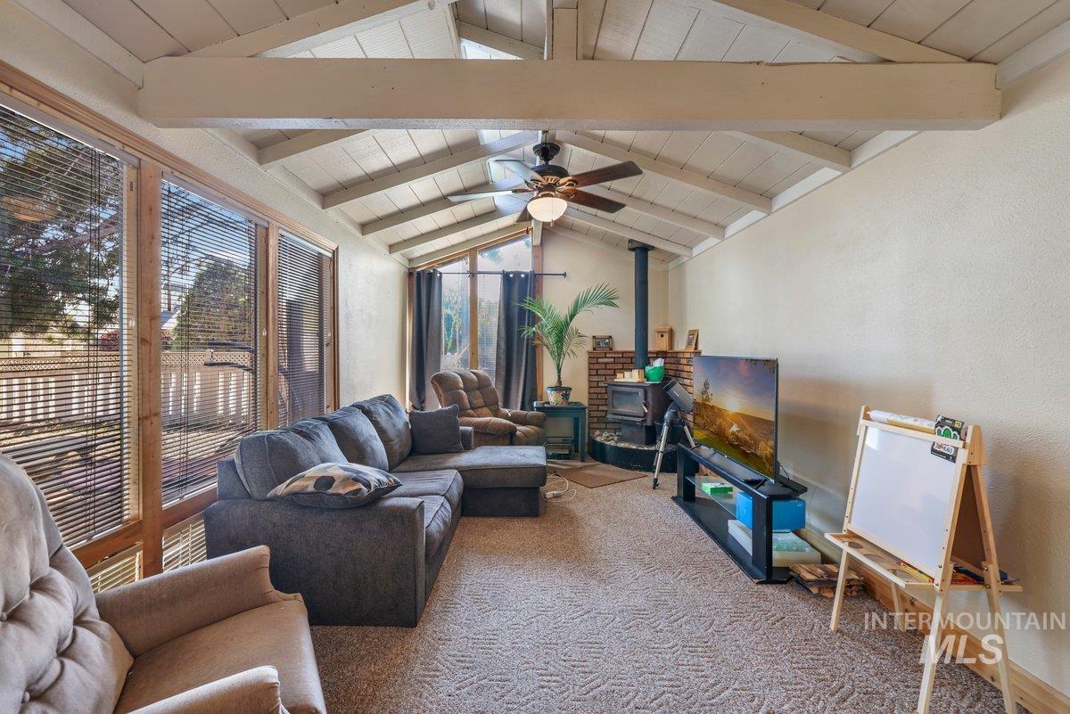 Carpeted living room with a wood stove, a ceiling fan, and wood ceiling