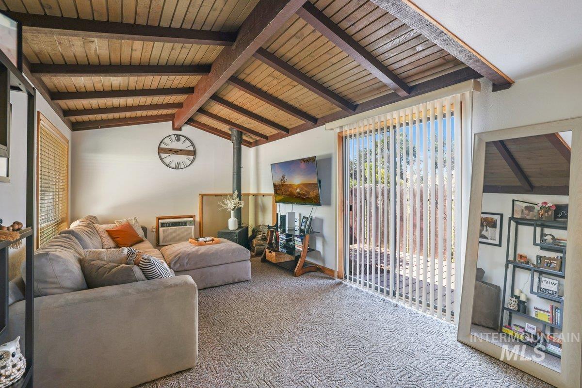 Carpeted living room featuring a wood stove, a wall mounted air conditioner, and wooden ceiling