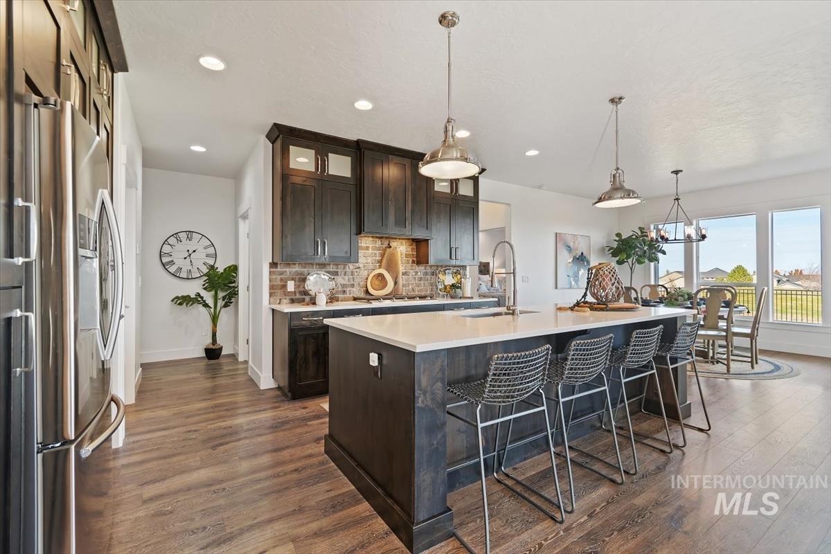 Kitchen featuring dark brown cabinets, backsplash, decorative light fixtures, a kitchen breakfast bar, and stainless steel fridge with ice dispenser
