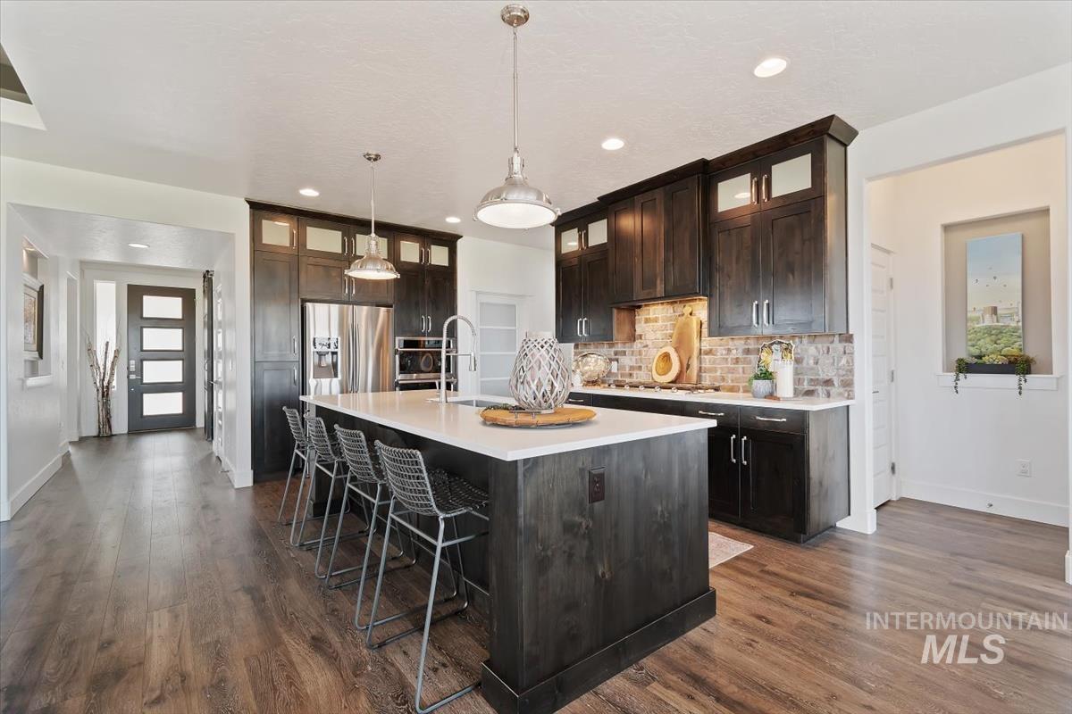 Kitchen featuring dark brown cabinets, a kitchen breakfast bar, a center island with sink, backsplash, and dark wood-style flooring