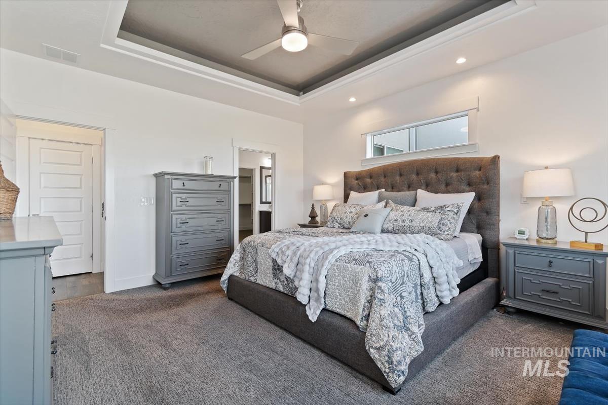 Bedroom featuring a raised ceiling, ensuite bath, dark carpet, ceiling fan, and recessed lighting