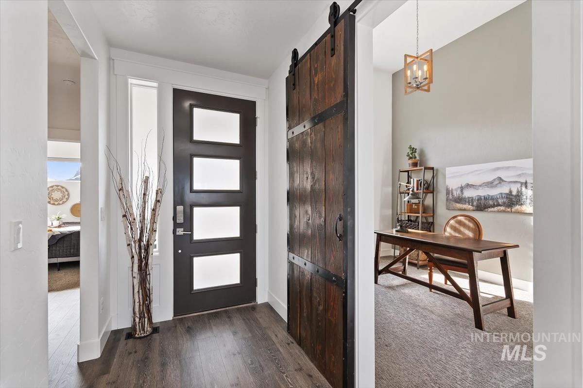 Entryway with a barn door, dark wood-type flooring, dark colored carpet, and a chandelier