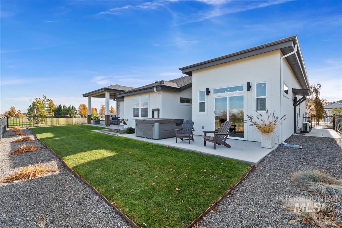 Rear view of property featuring a hot tub, a patio area, a fenced backyard, and stucco siding