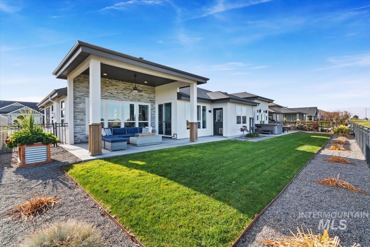 Rear view of house with a ceiling fan, a patio area, outdoor lounge area, stone siding, and a hot tub