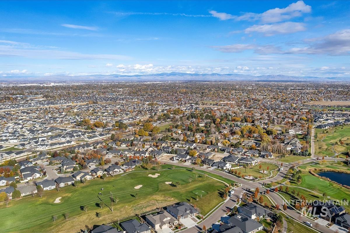 Aerial view of property and surrounding area featuring a golf club, nearby suburban area, and a water and mountain view