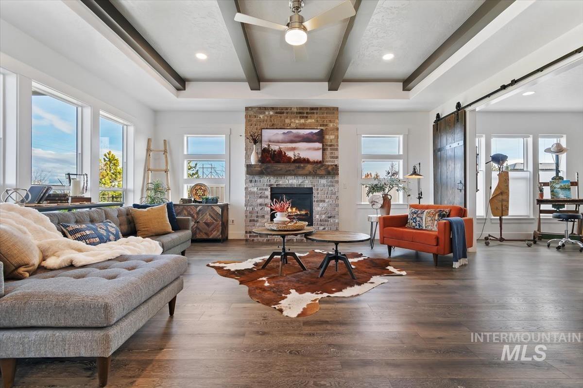 Living room featuring a barn door, wood finished floors, beamed ceiling, a fireplace, and a ceiling fan