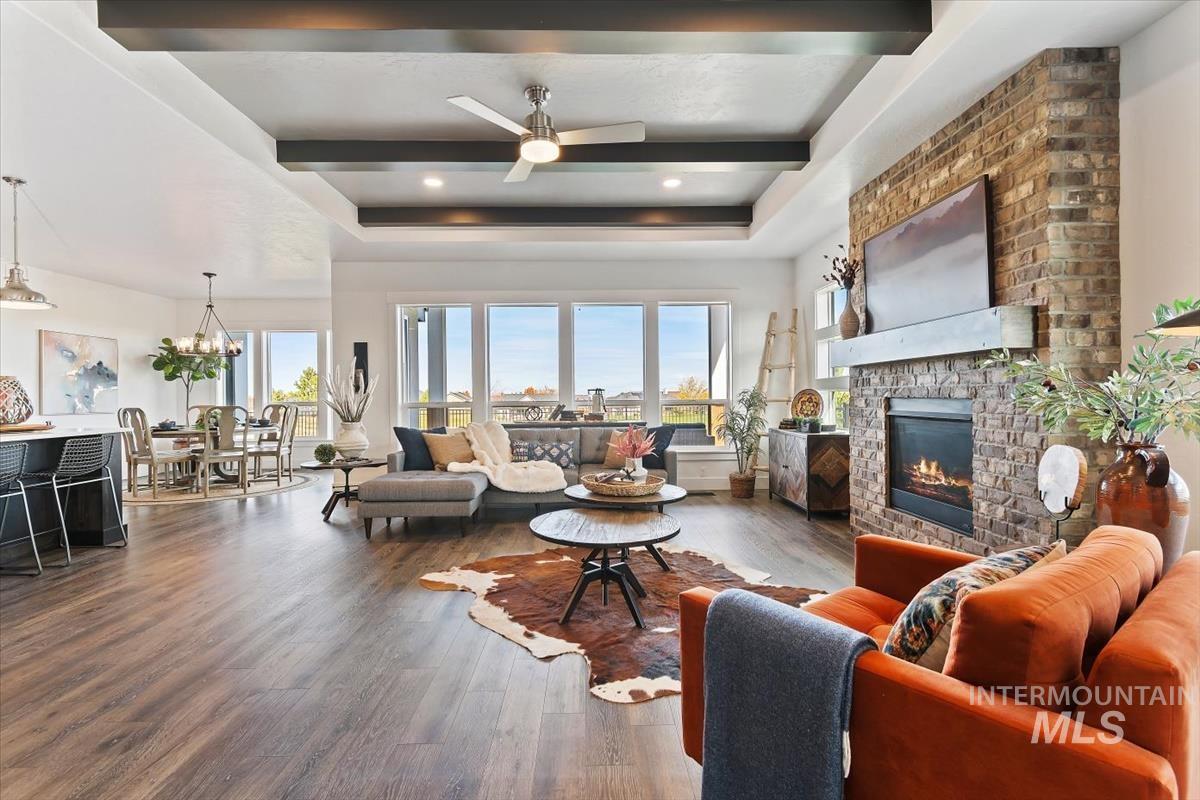 Living room with a ceiling fan, a large fireplace, wood finished floors, a raised ceiling, and beam ceiling
