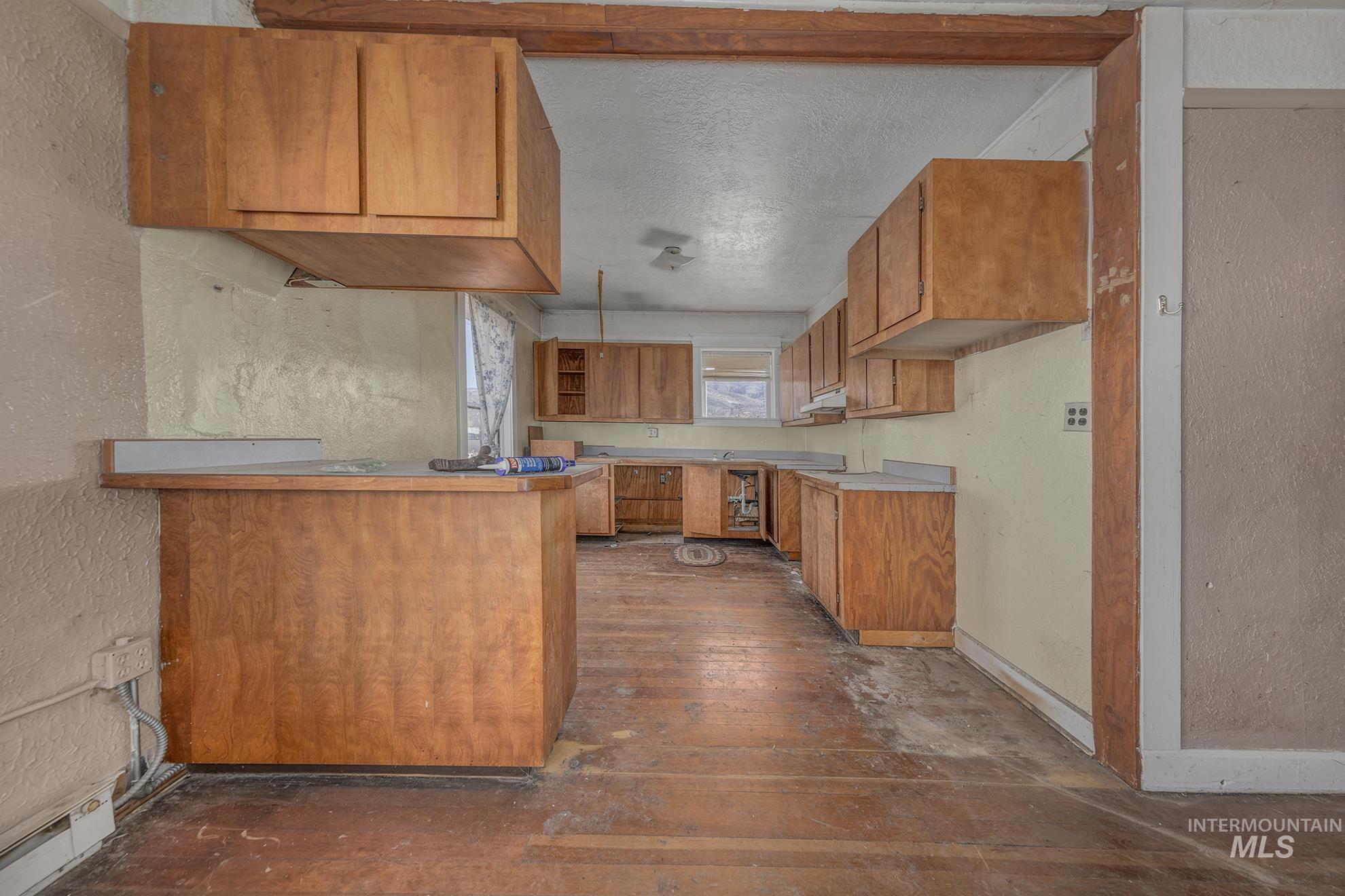 Kitchen featuring a textured wall, brown cabinets, a textured ceiling, a peninsula, and a baseboard heating unit
