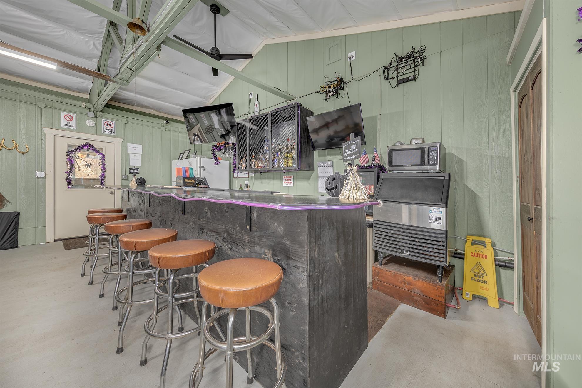 Community bar area with wooden walls, lofted ceiling, stainless steel microwave, and dark countertops