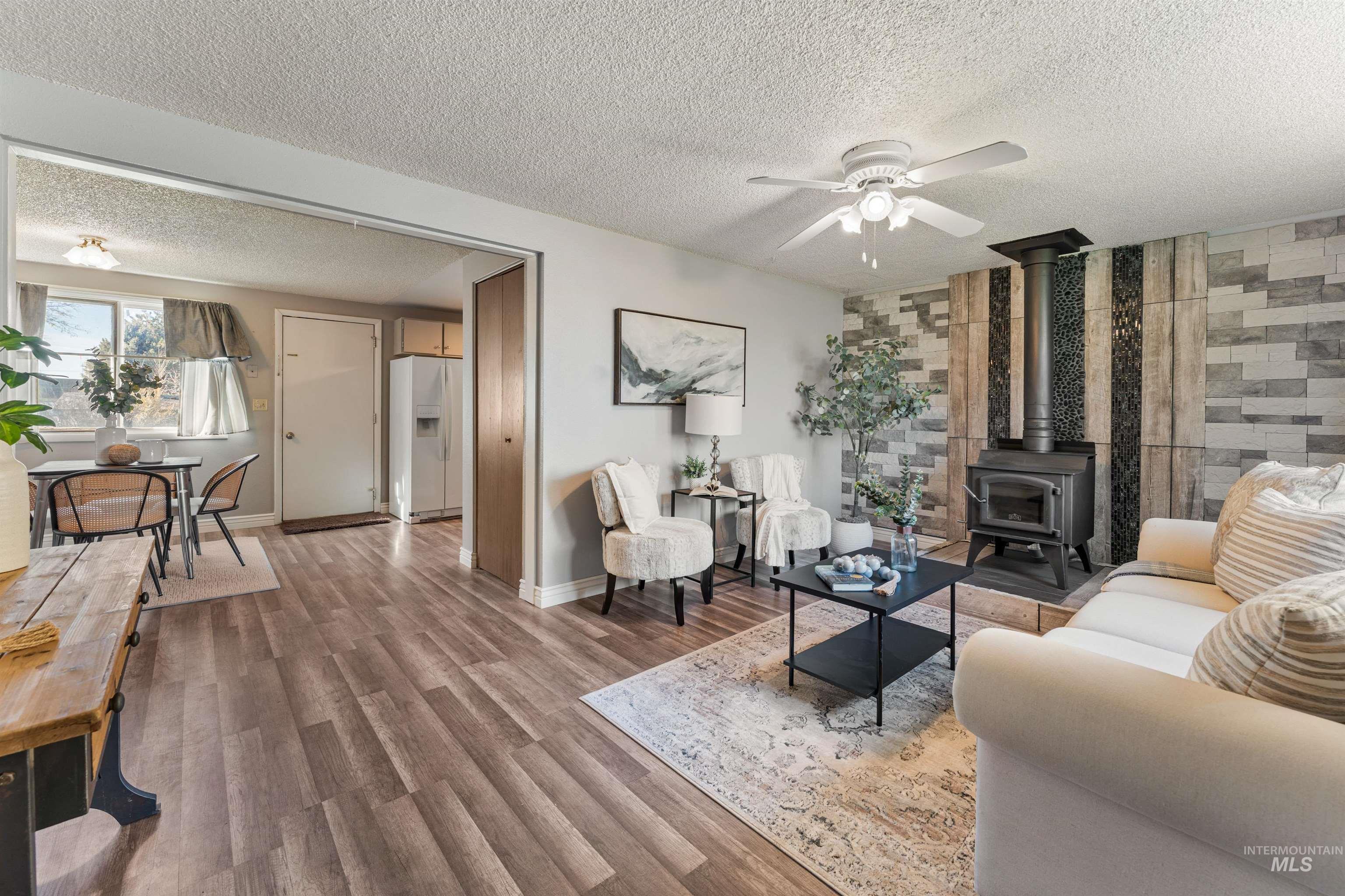Living room with a wood stove, wood finished floors, ceiling fan, and a textured ceiling