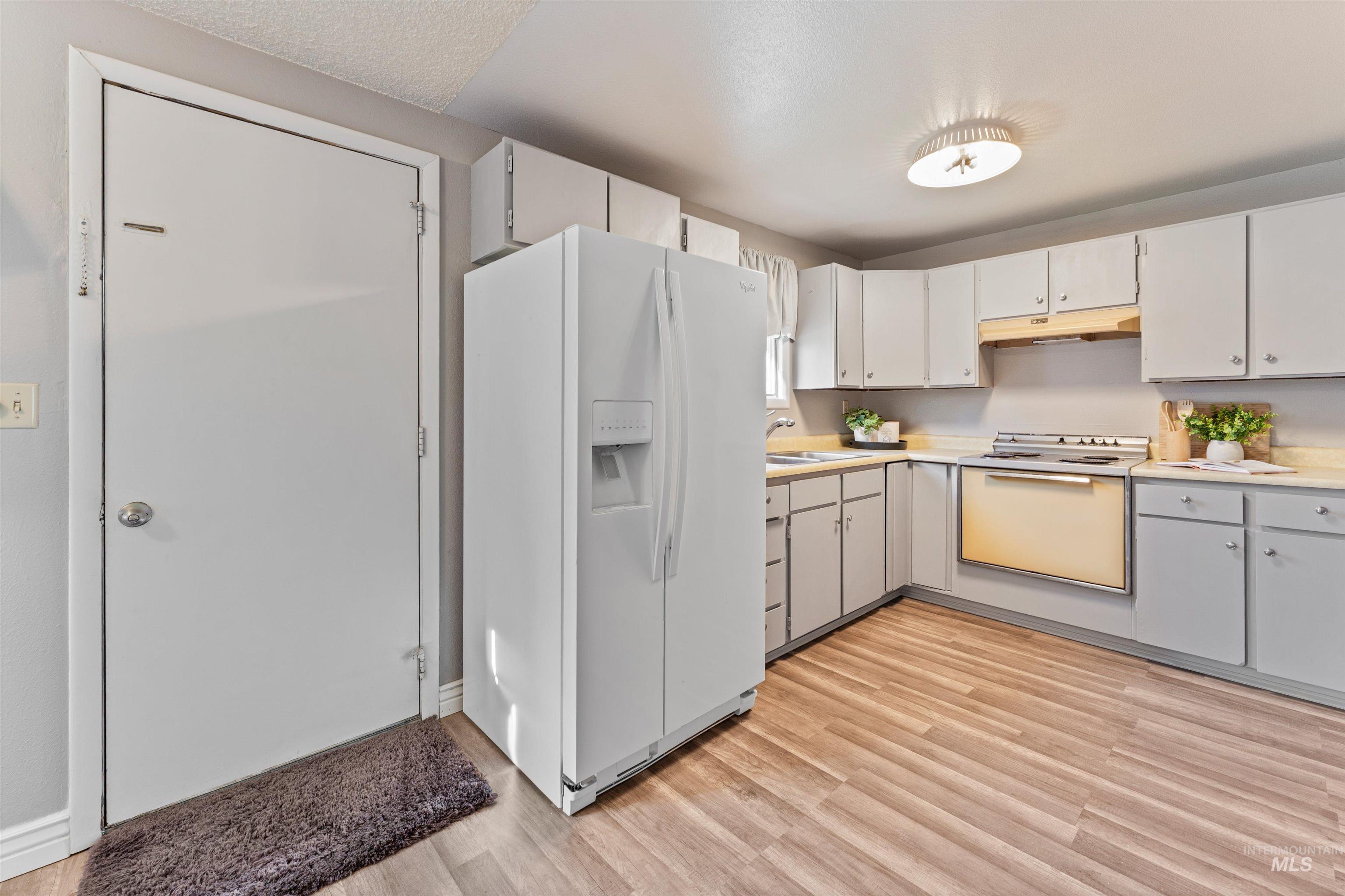 Kitchen featuring white appliances, light countertops, light wood-style flooring, under cabinet range hood, and white cabinetry