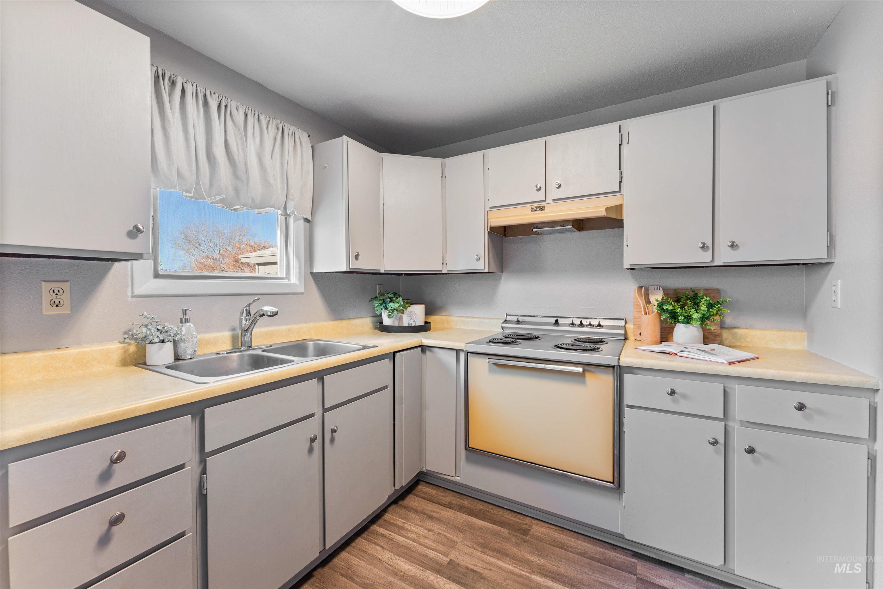 Kitchen featuring range with electric stovetop, light countertops, dark wood-style floors, and under cabinet range hood