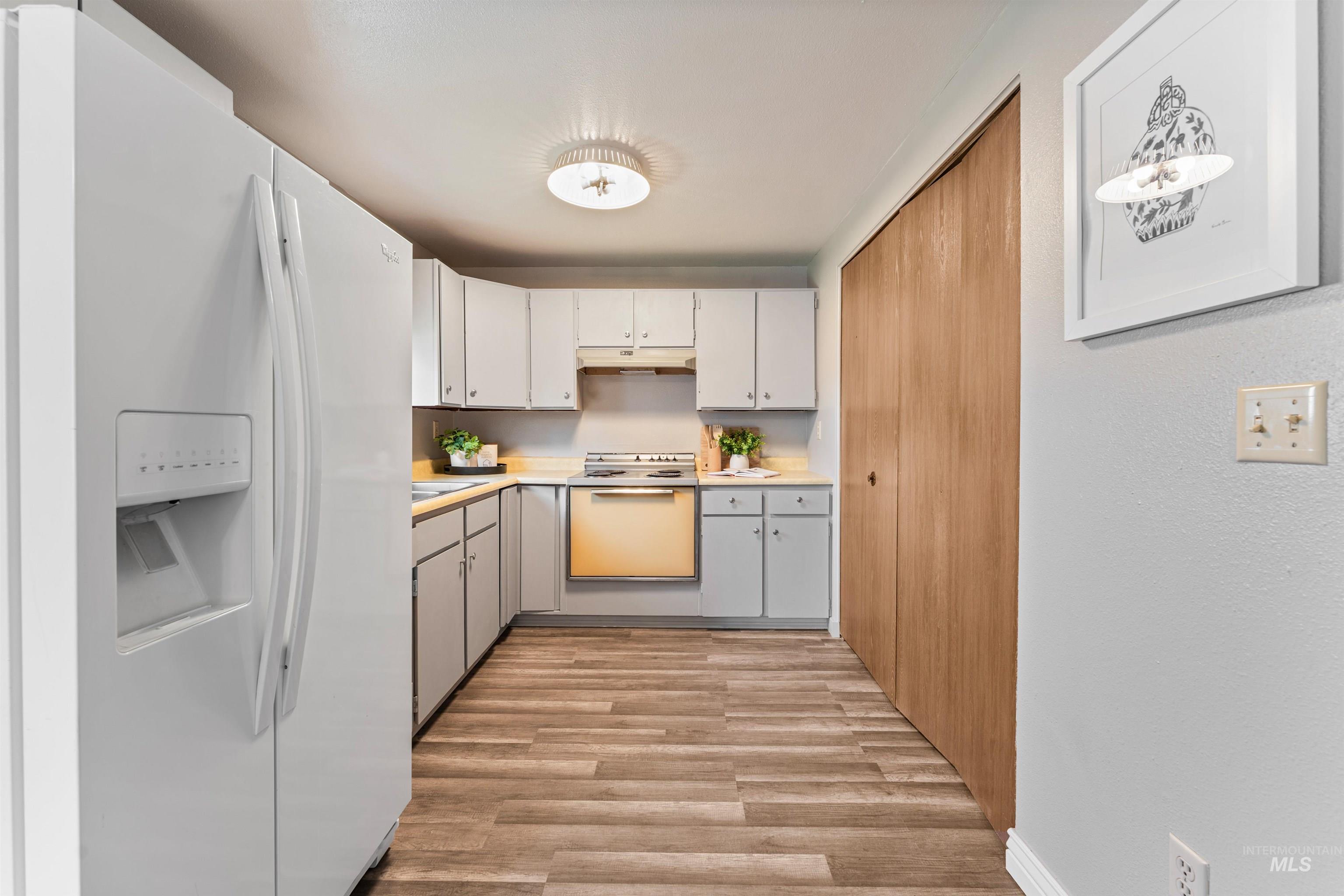 Kitchen featuring white appliances, light countertops, white cabinetry, light wood-style flooring, and under cabinet range hood