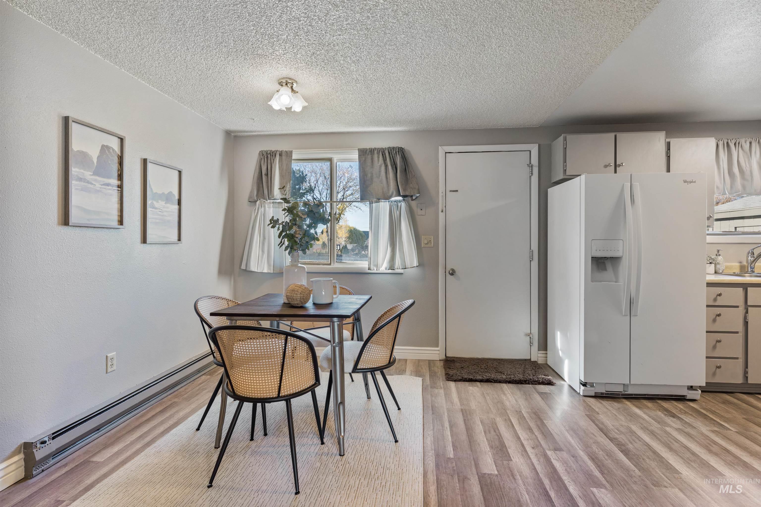 Dining space featuring baseboard heating, light wood-type flooring, and a textured ceiling