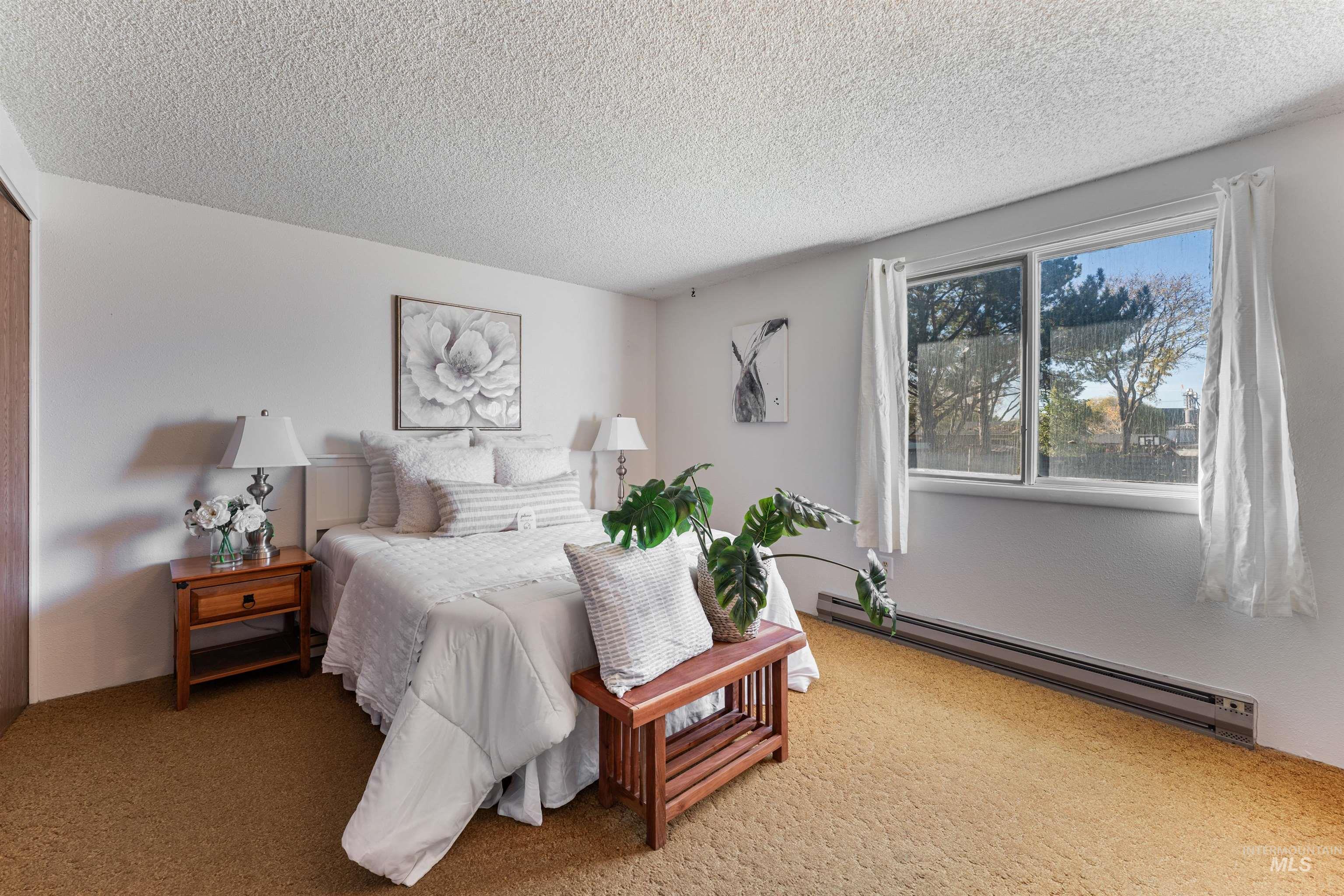Carpeted bedroom with a baseboard heating unit and a textured ceiling