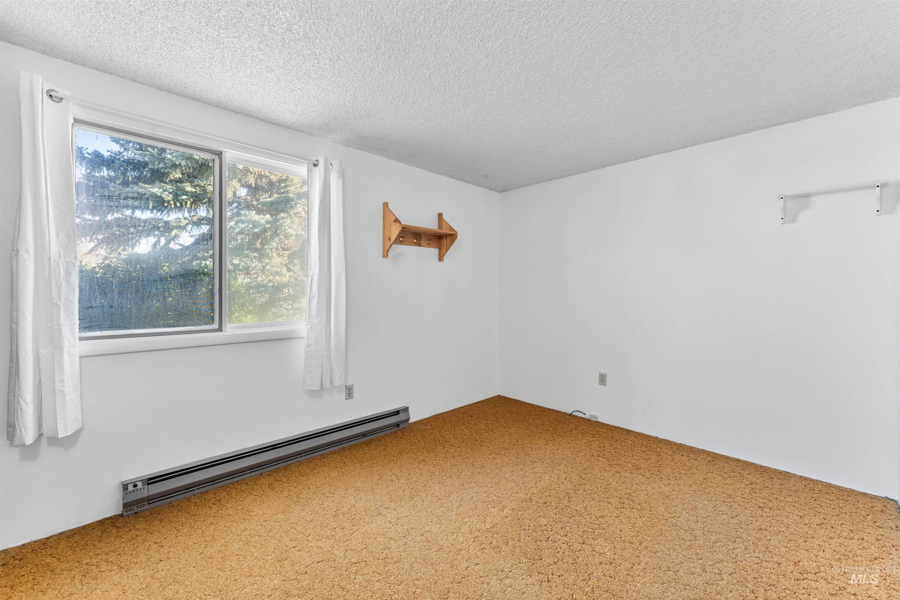 Carpeted empty room featuring a baseboard heating unit and a textured ceiling