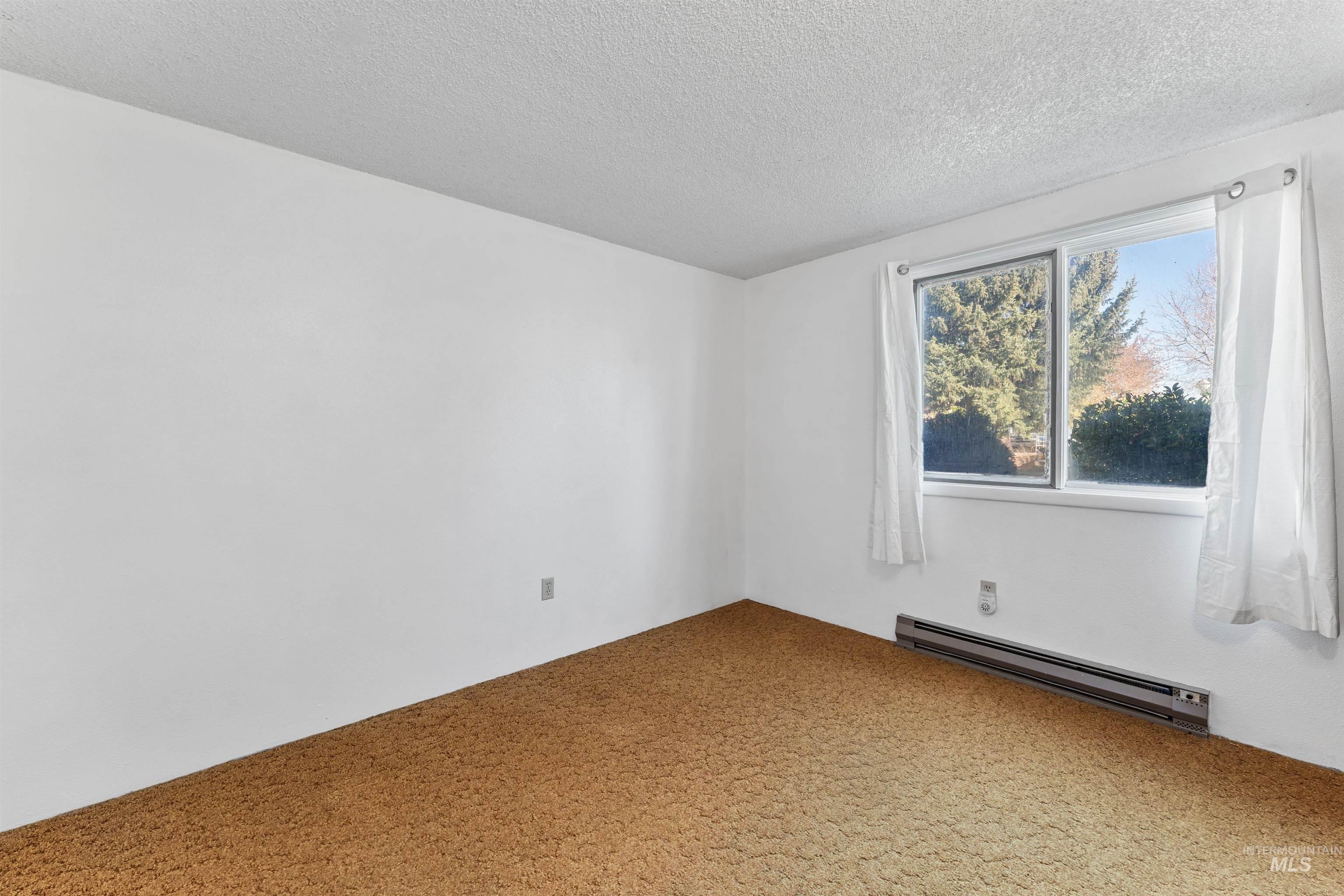 Carpeted spare room featuring a baseboard heating unit and a textured ceiling