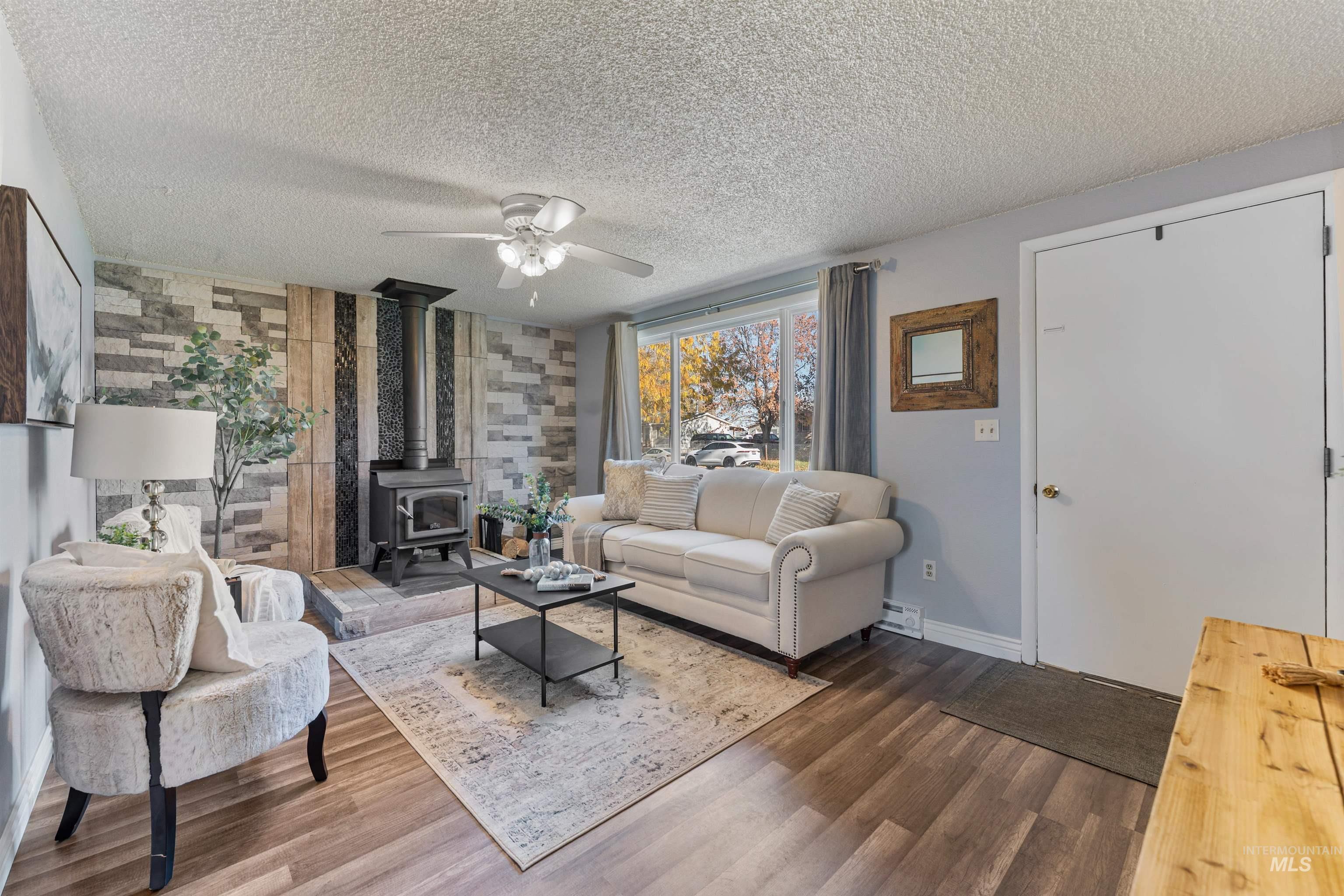Living room with a wood stove, a ceiling fan, wood finished floors, and a textured ceiling
