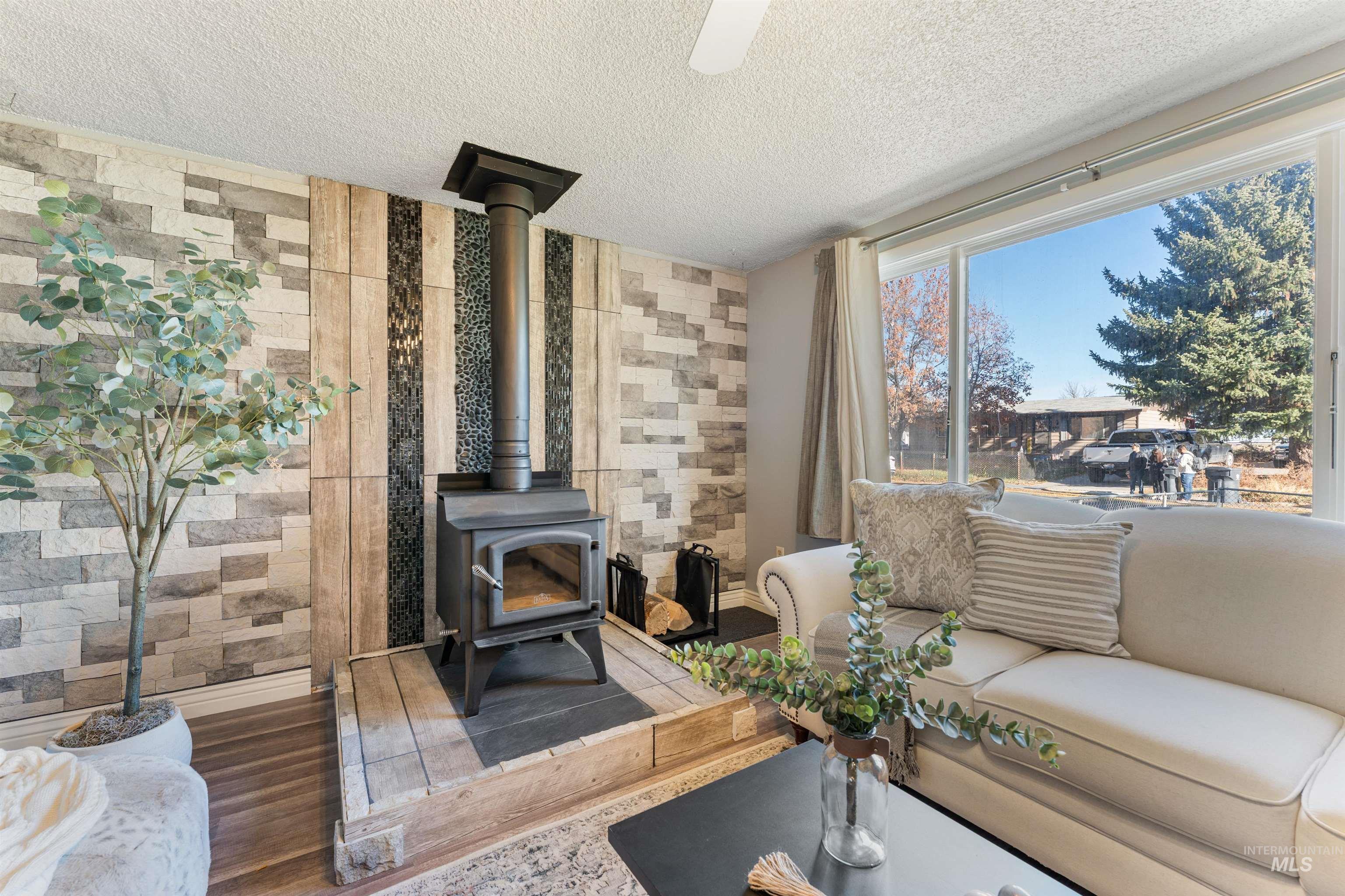 Living room with a wood stove, a textured ceiling, wood finished floors, and tile walls