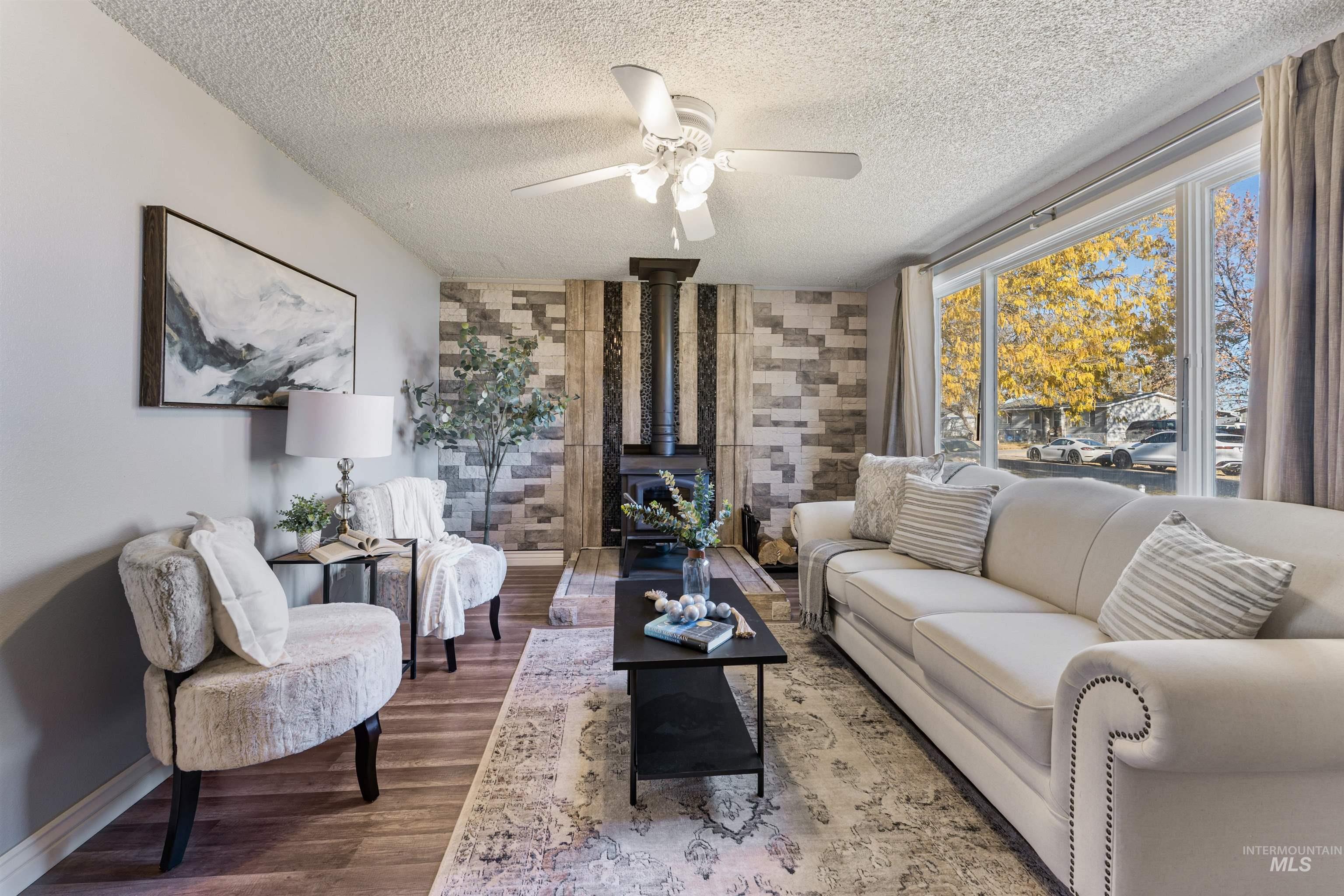Living area featuring a wood stove, wood finished floors, ceiling fan, and a textured ceiling