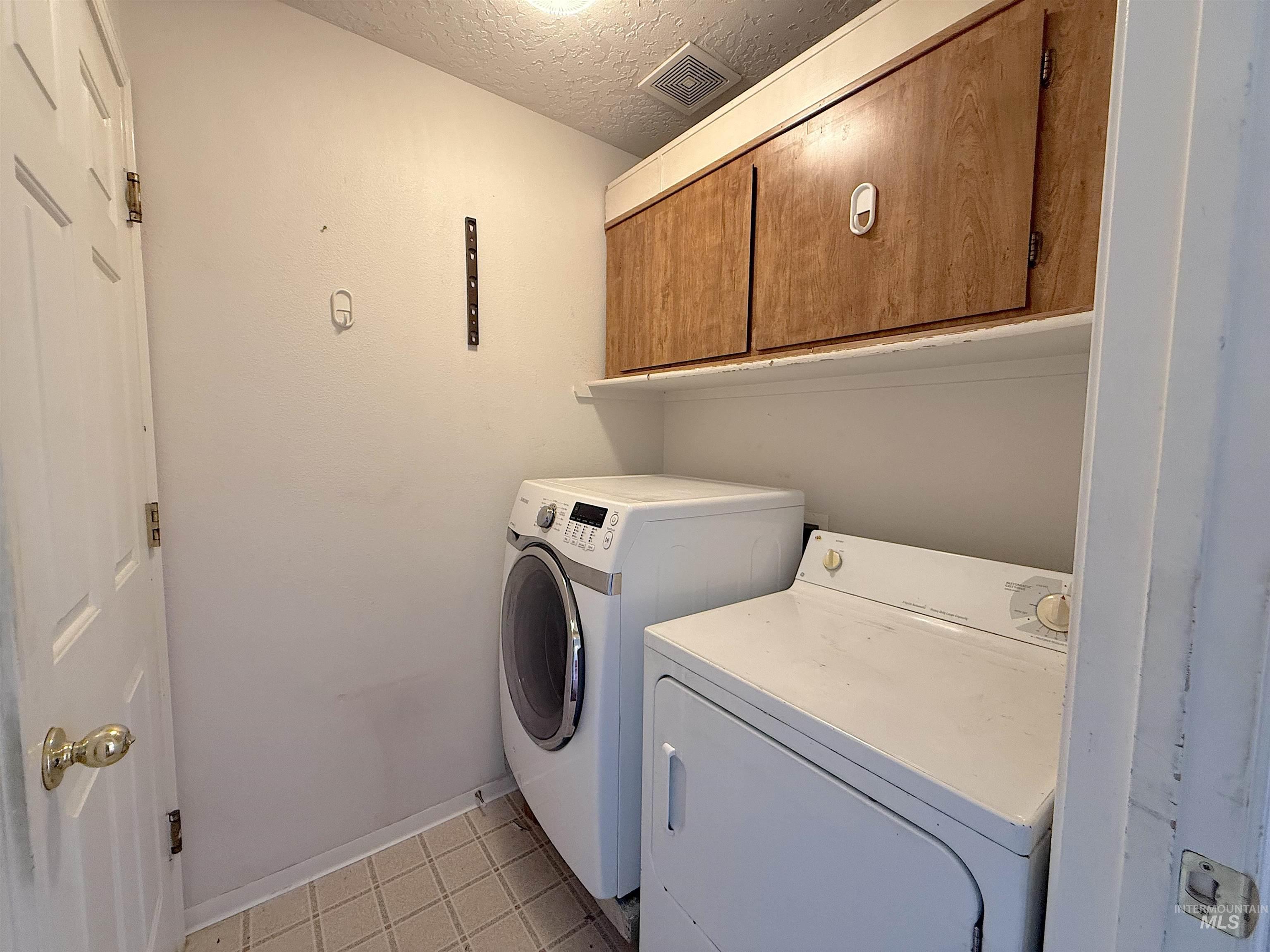 Laundry area with a textured ceiling, washer and clothes dryer, and cabinet space