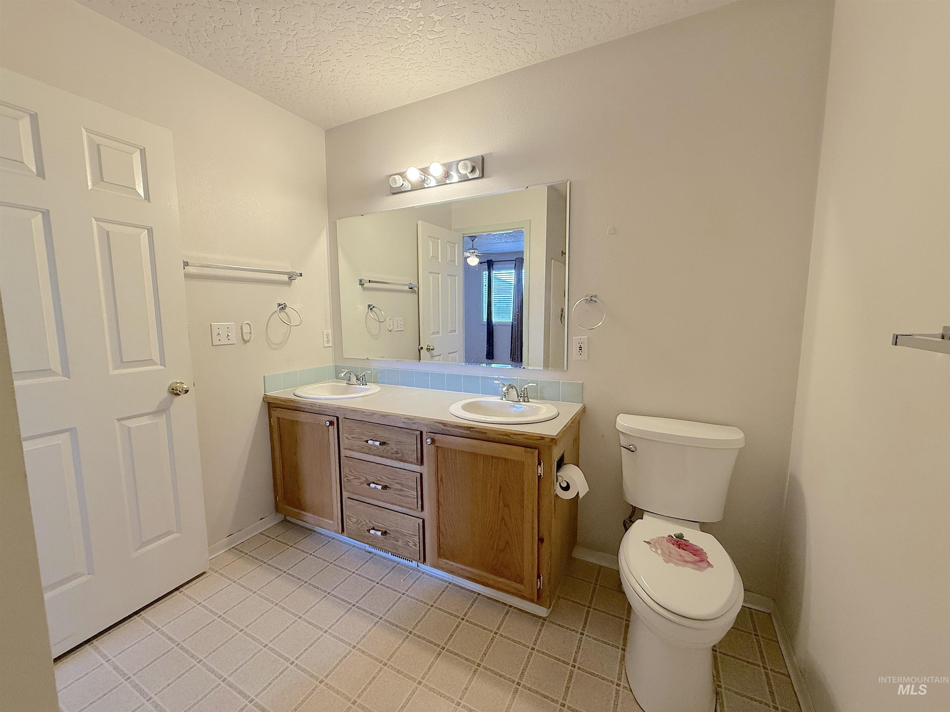 Full bathroom with double vanity, a textured ceiling, and light tile patterned floors