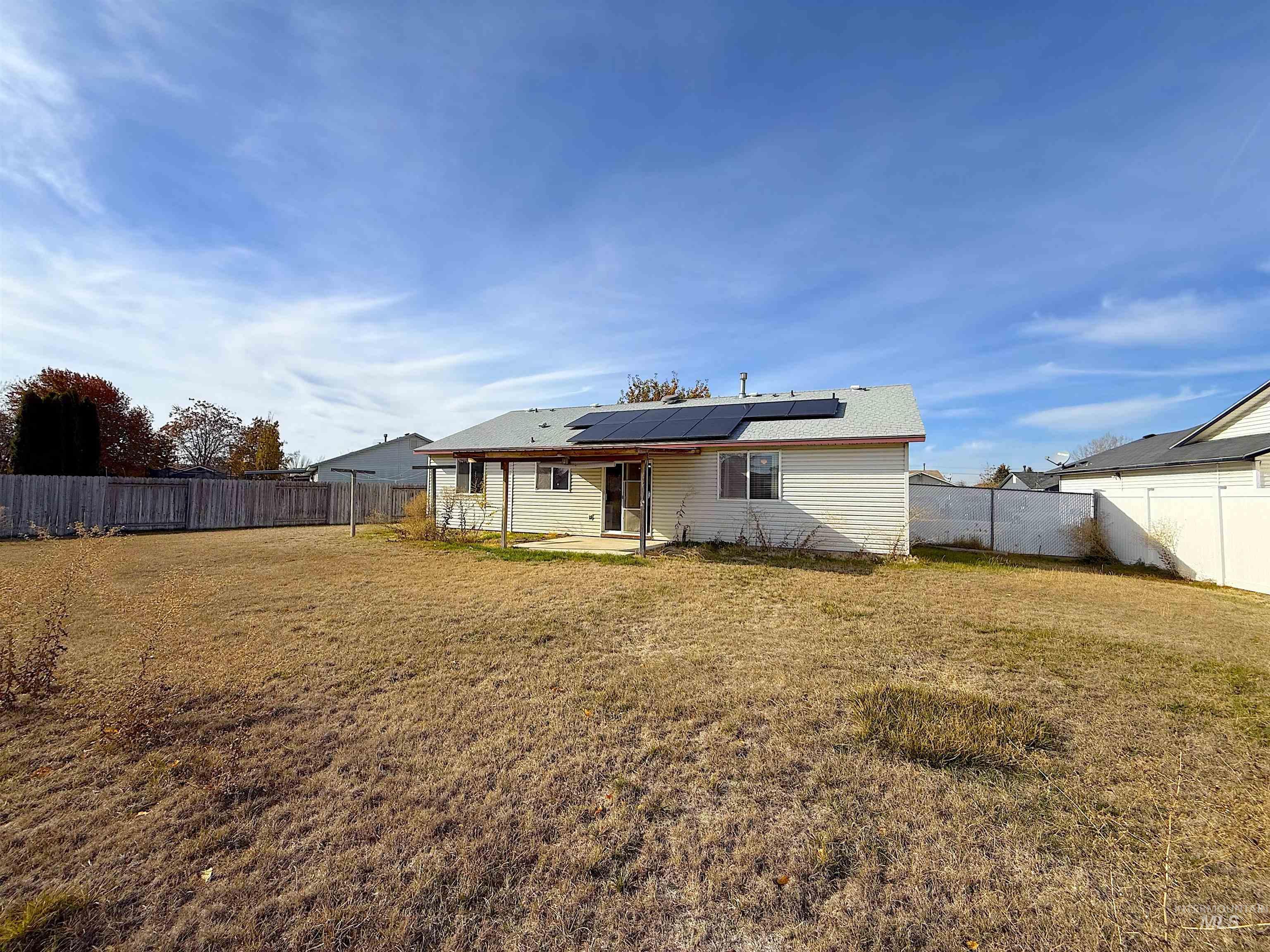 Back of property with a patio, roof mounted solar panels, and a fenced backyard