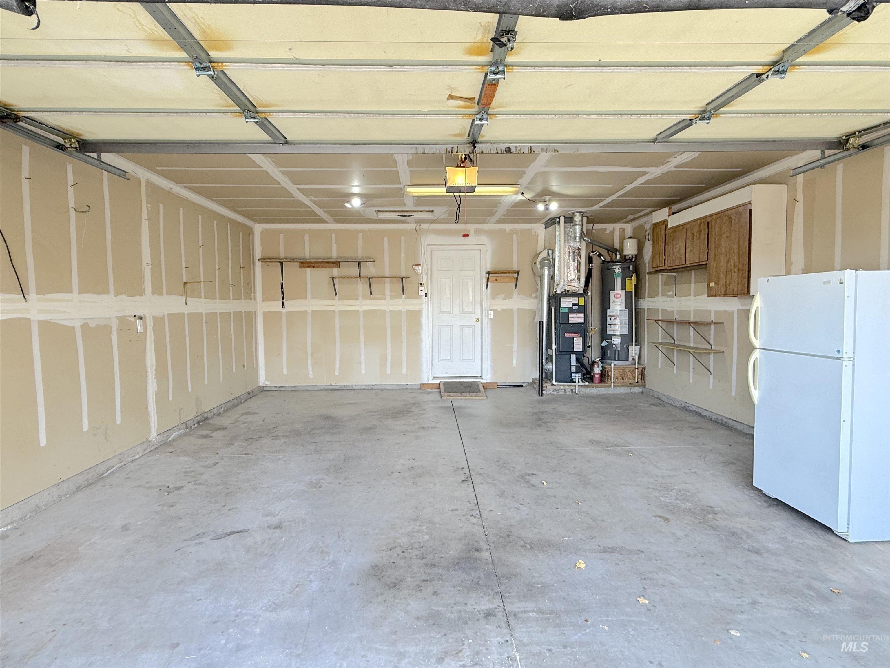 Garage with freestanding refrigerator, gas water heater, a garage door opener, and heating unit