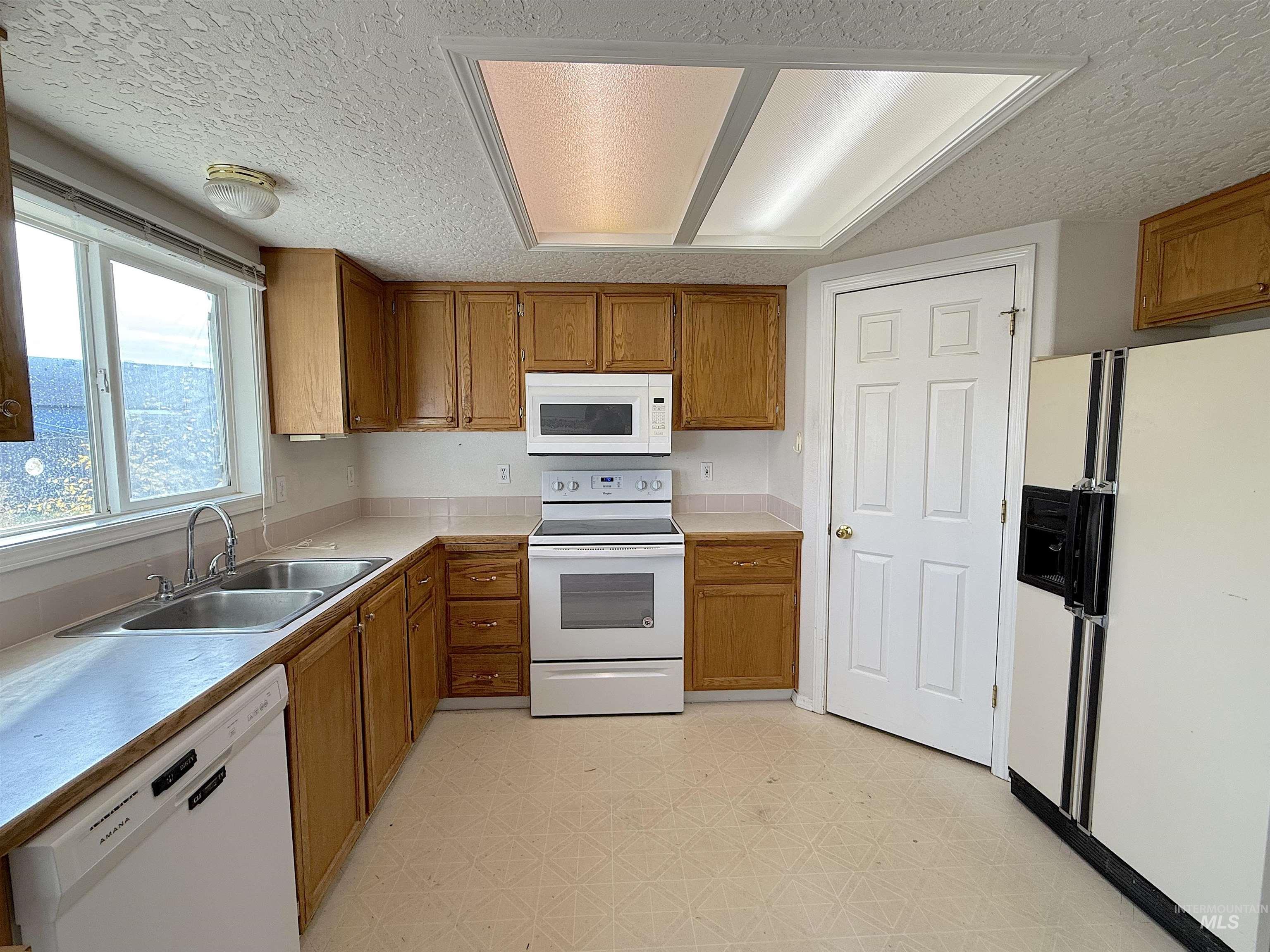 Kitchen featuring white appliances, light countertops, a textured ceiling, brown cabinetry, and light flooring