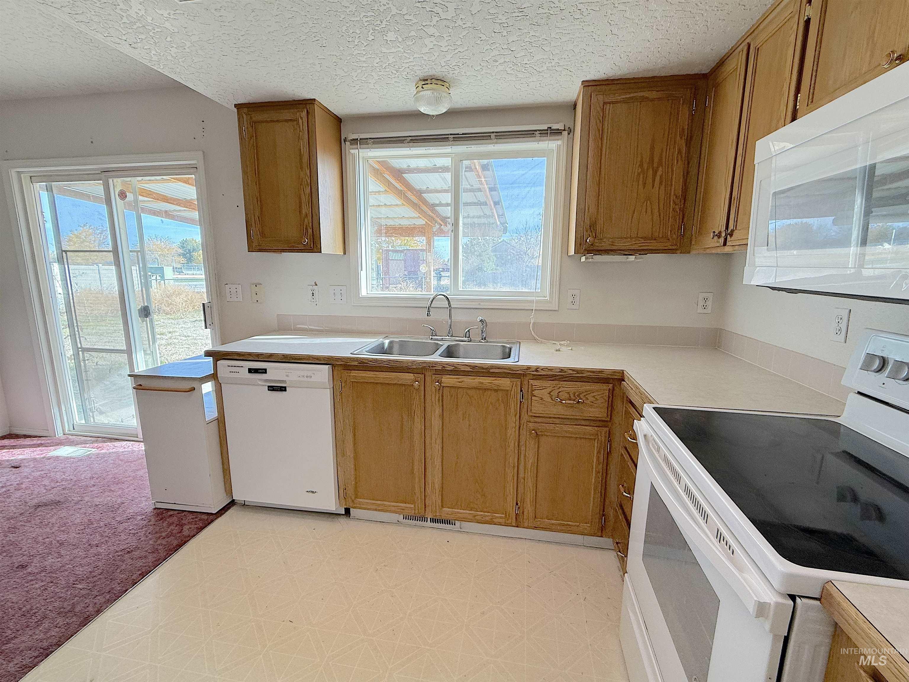 Kitchen featuring white appliances, light countertops, a textured ceiling, brown cabinets, and light flooring