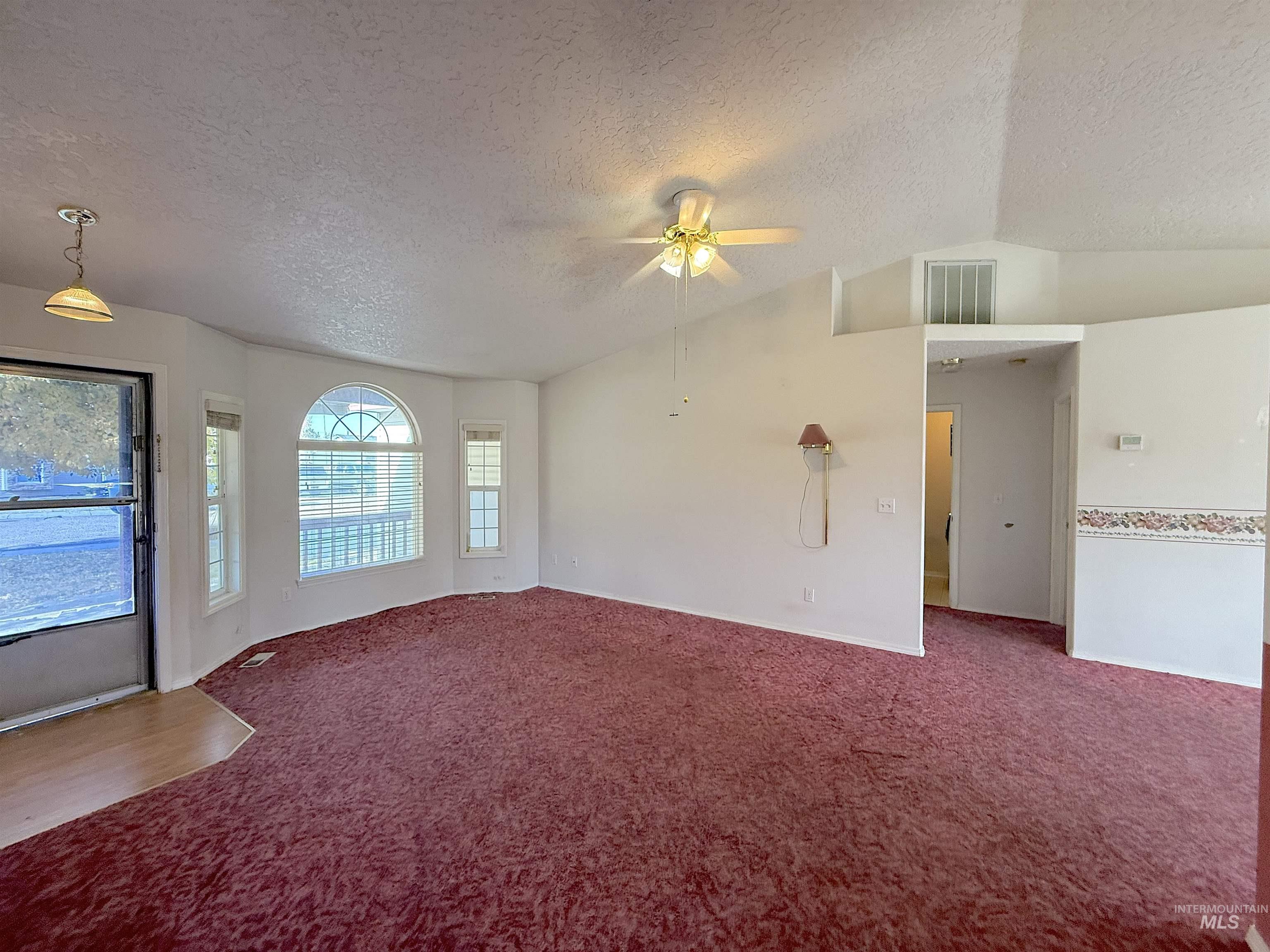 Unfurnished living room featuring a textured ceiling, vaulted ceiling, carpet, and a ceiling fan