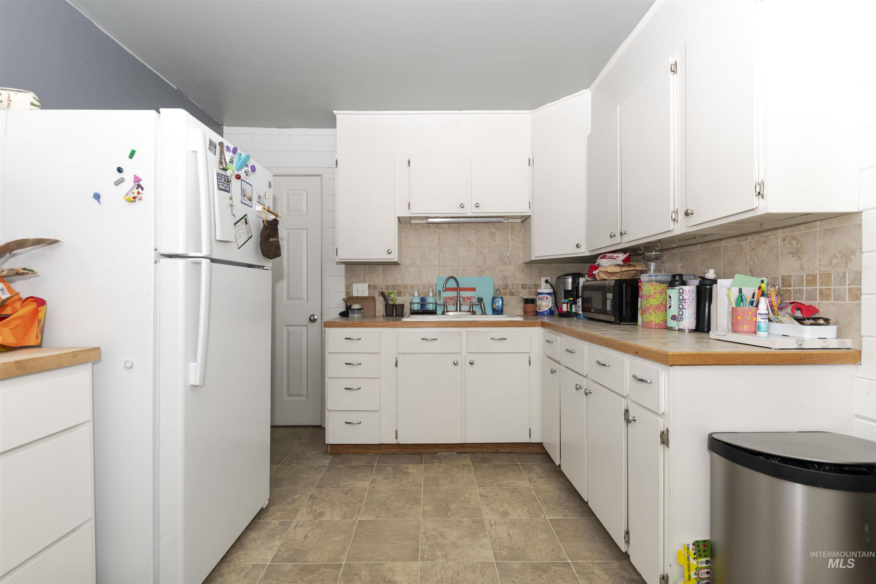 Kitchen with freestanding refrigerator, white cabinetry, backsplash, and black microwave