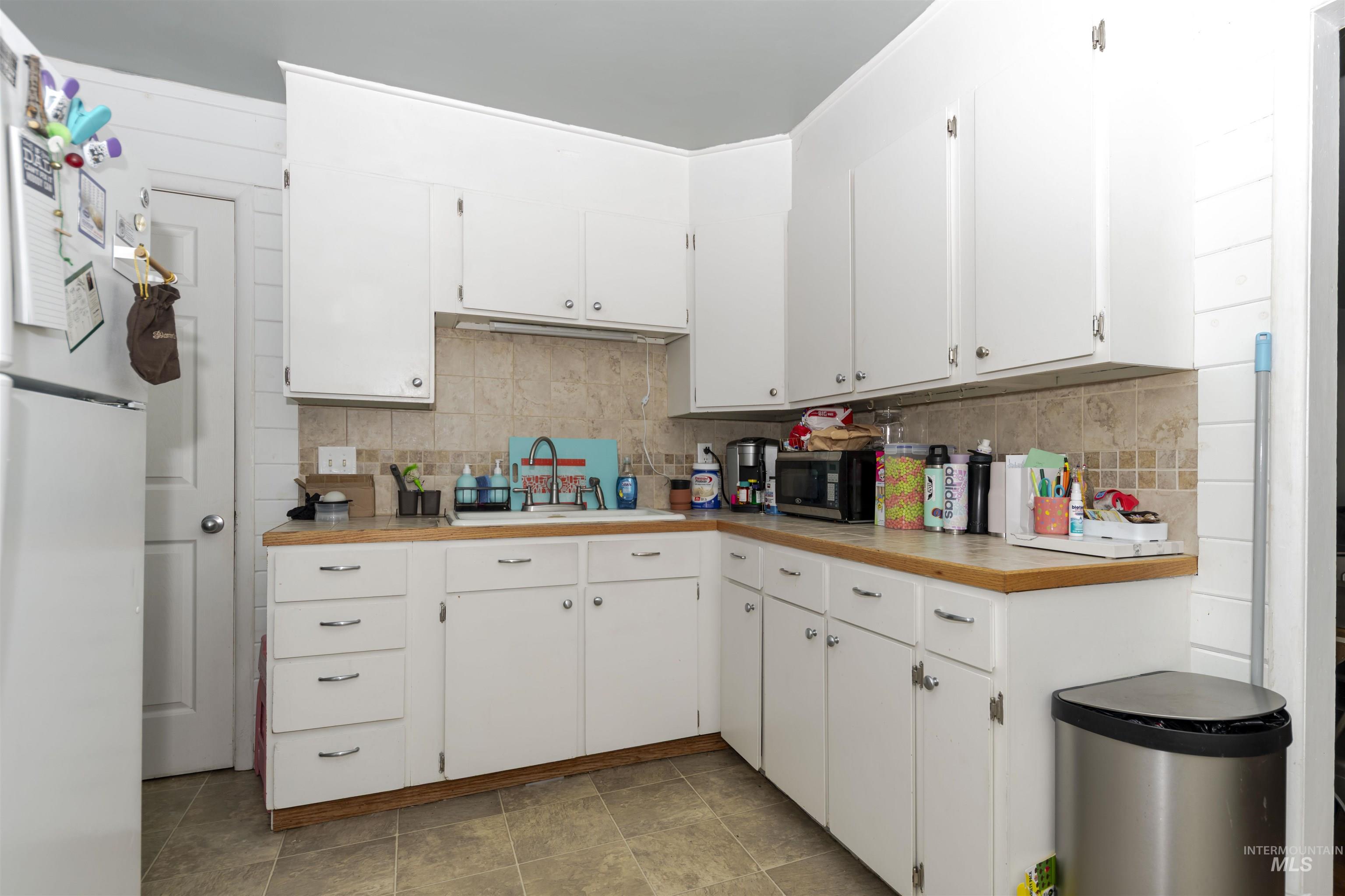 Kitchen featuring freestanding refrigerator, white cabinets, and decorative backsplash